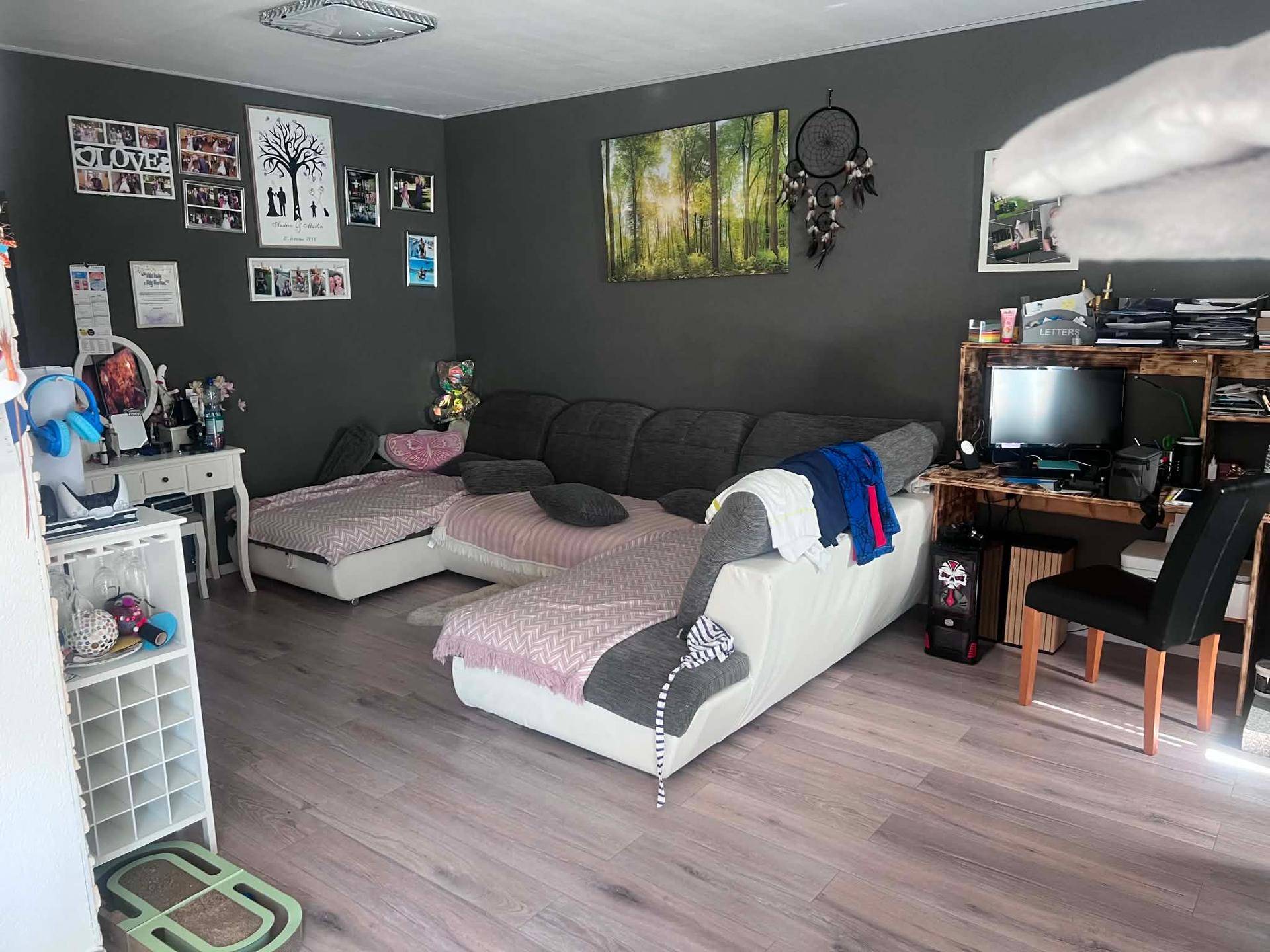 Geräumiges Wohnzimmer mit großem Ecksofa, dunklen Wänden und modernem Laminatboden.