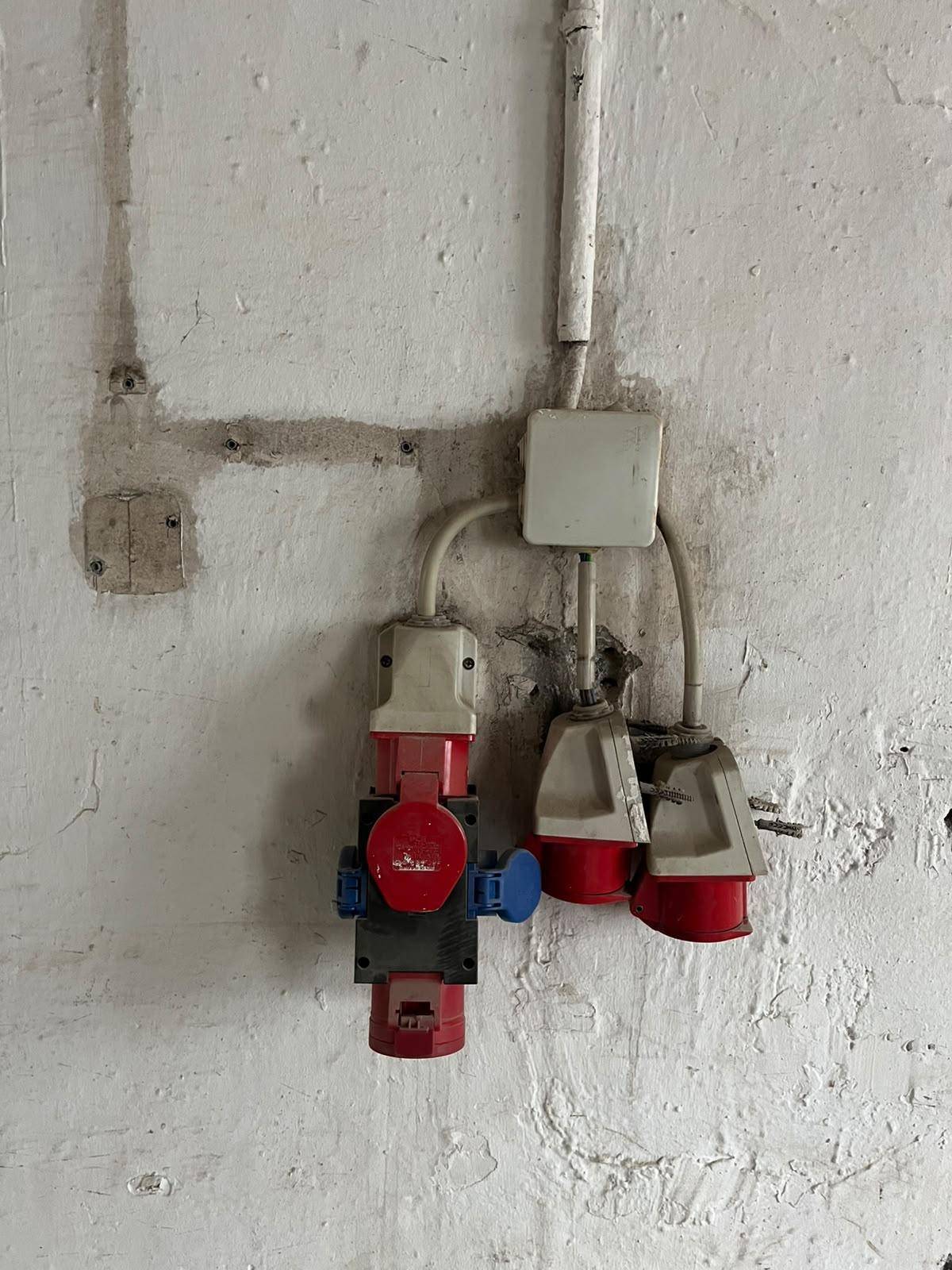 Nahaufnahme von roten Industriesteckdosen und Verkabelung an einer rauen Wand.