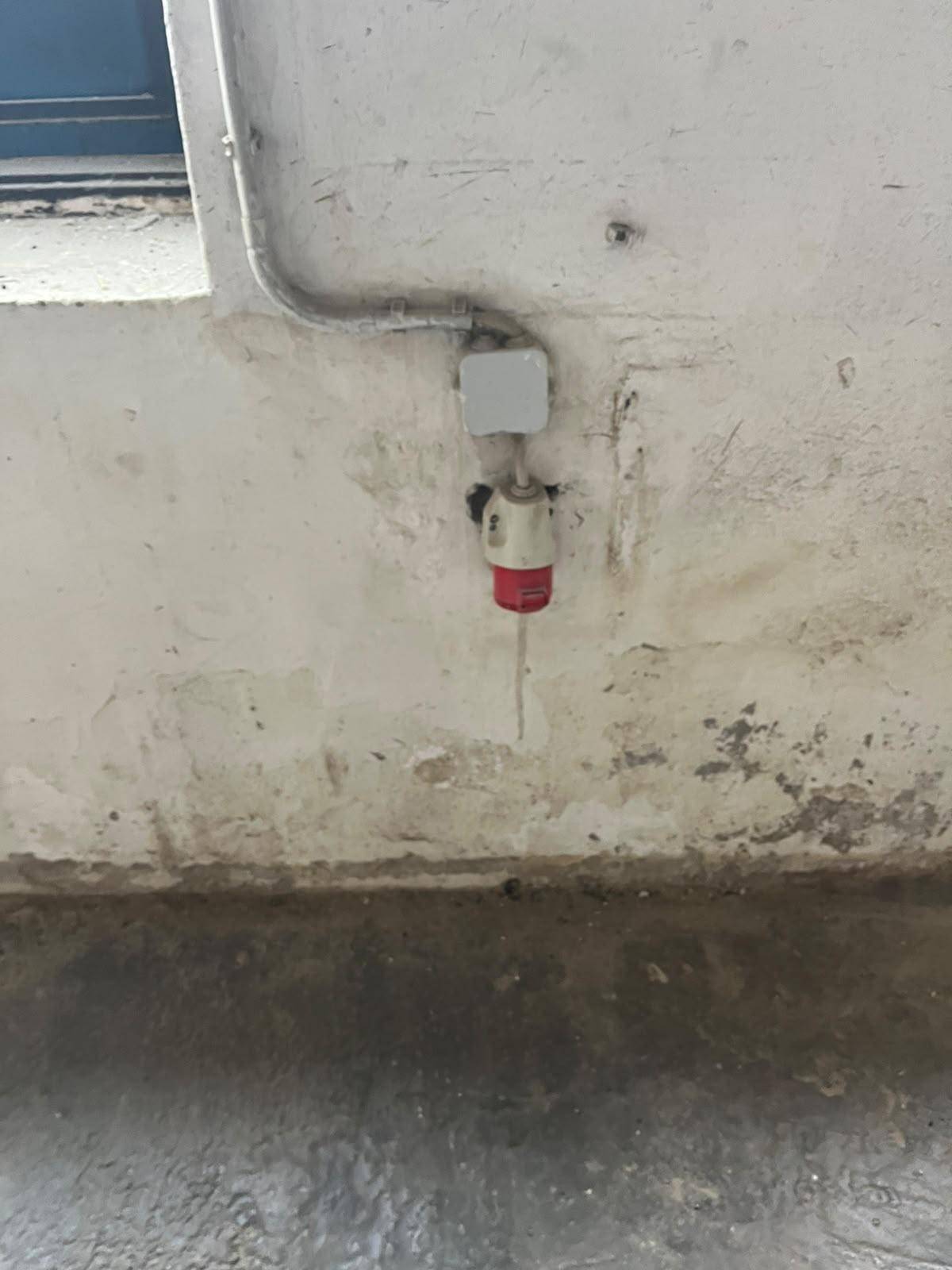 Einzelne rote Industriesteckdose mit sichtbarer Verkabelung an einer abgenutzten Wand.
