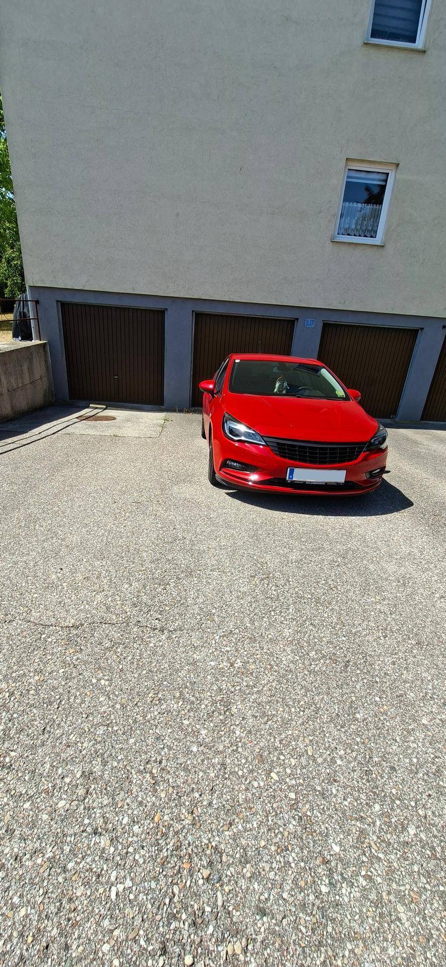 Außenbereich mit Garagentoren und einem geparkten roten Auto auf dem asphaltierten Vorplatz.