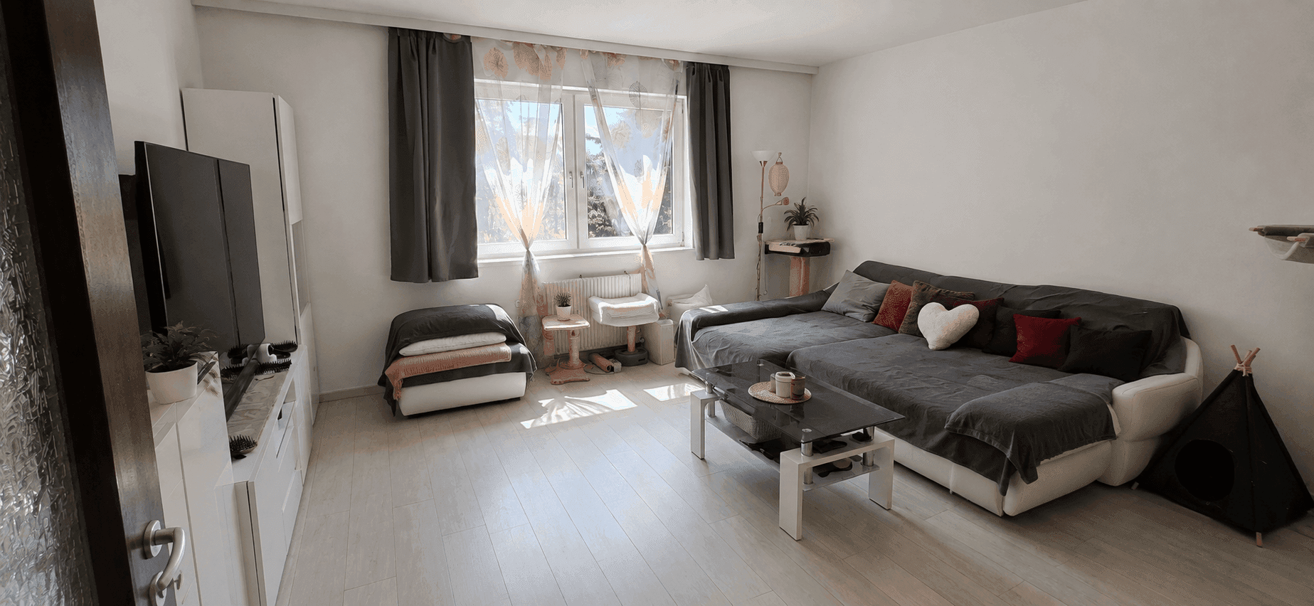 Helles Wohnzimmer mit großem Sofa, Laminatboden und Blick ins Grüne durch die Fenster.