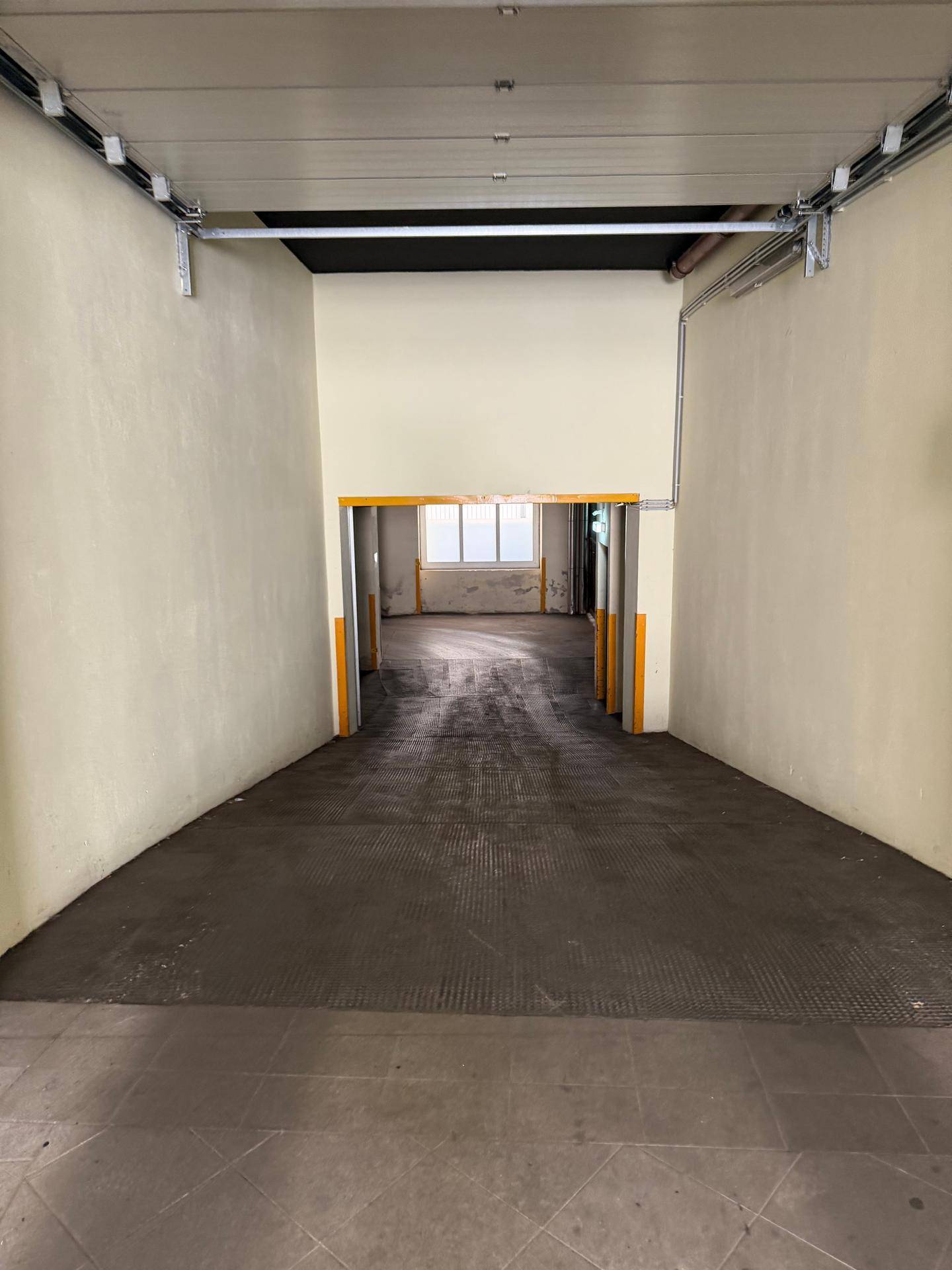 Lange Zufahrtsrampe zu einer Tiefgarage mit hellen Wänden und Betonboden.