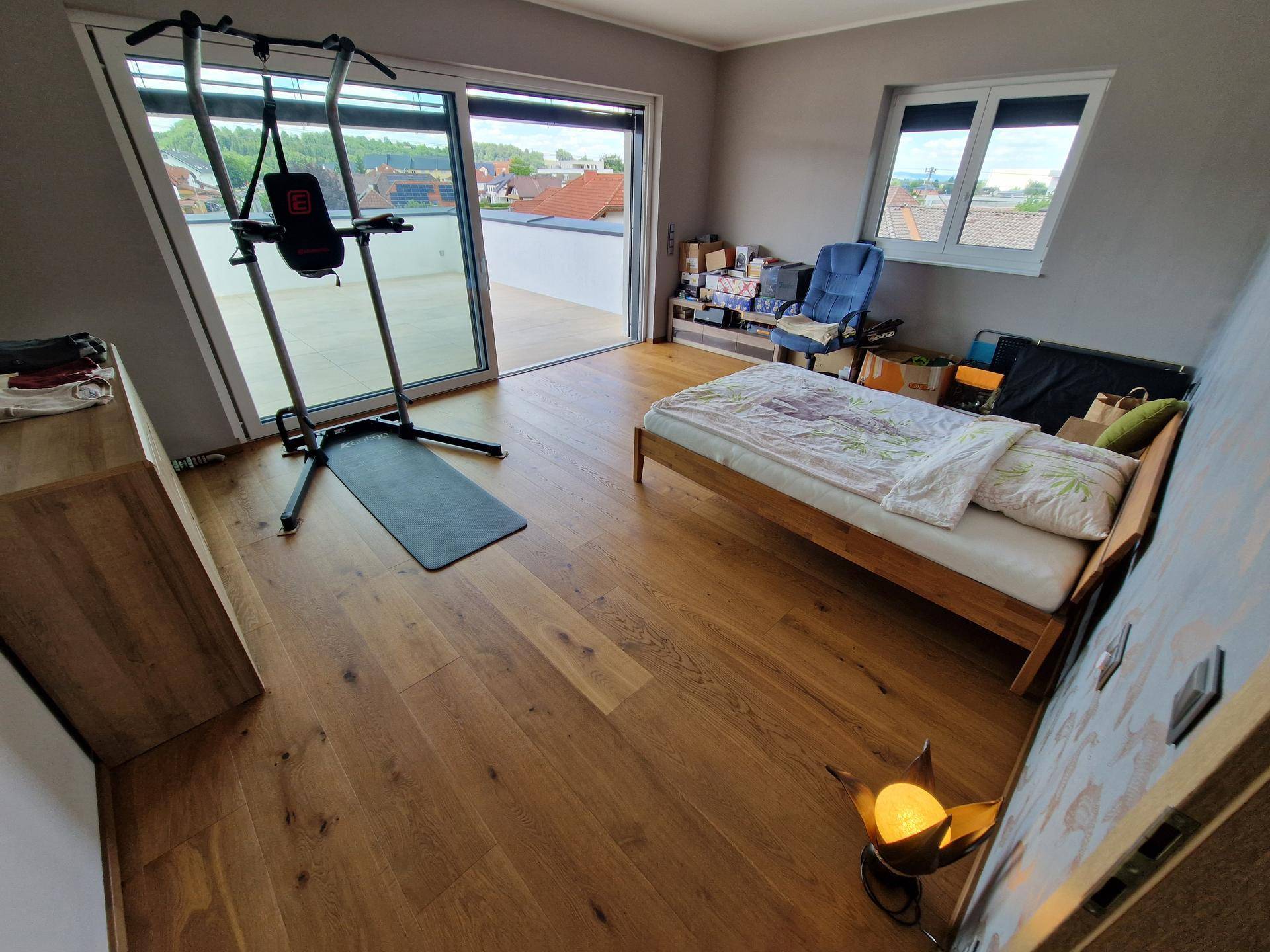 Schlafzimmer mit Holzboden, Einzelbett, Fitnessgerät und direktem Zugang zur Terrasse.