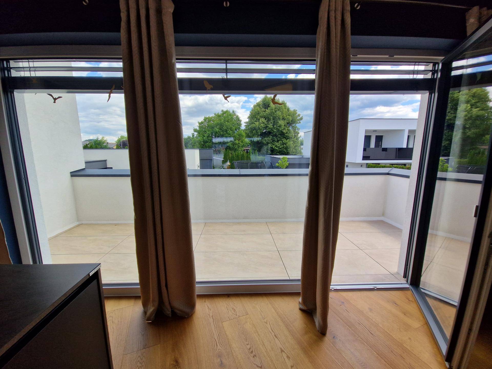 Blick aus dem Innenraum auf die Terrasse durch große Glastüren mit Vorhängen.