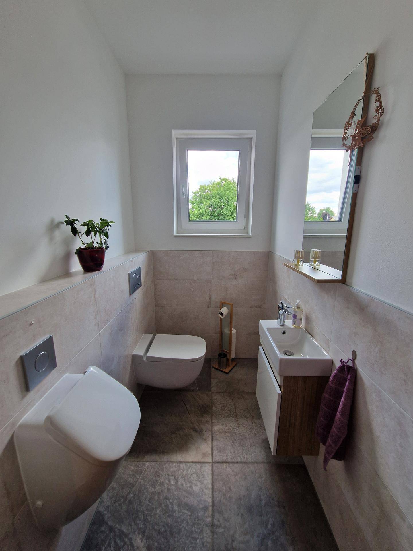 Modernes Gäste-WC mit wandhängender Toilette, Urinal und Fenster für Tageslicht.