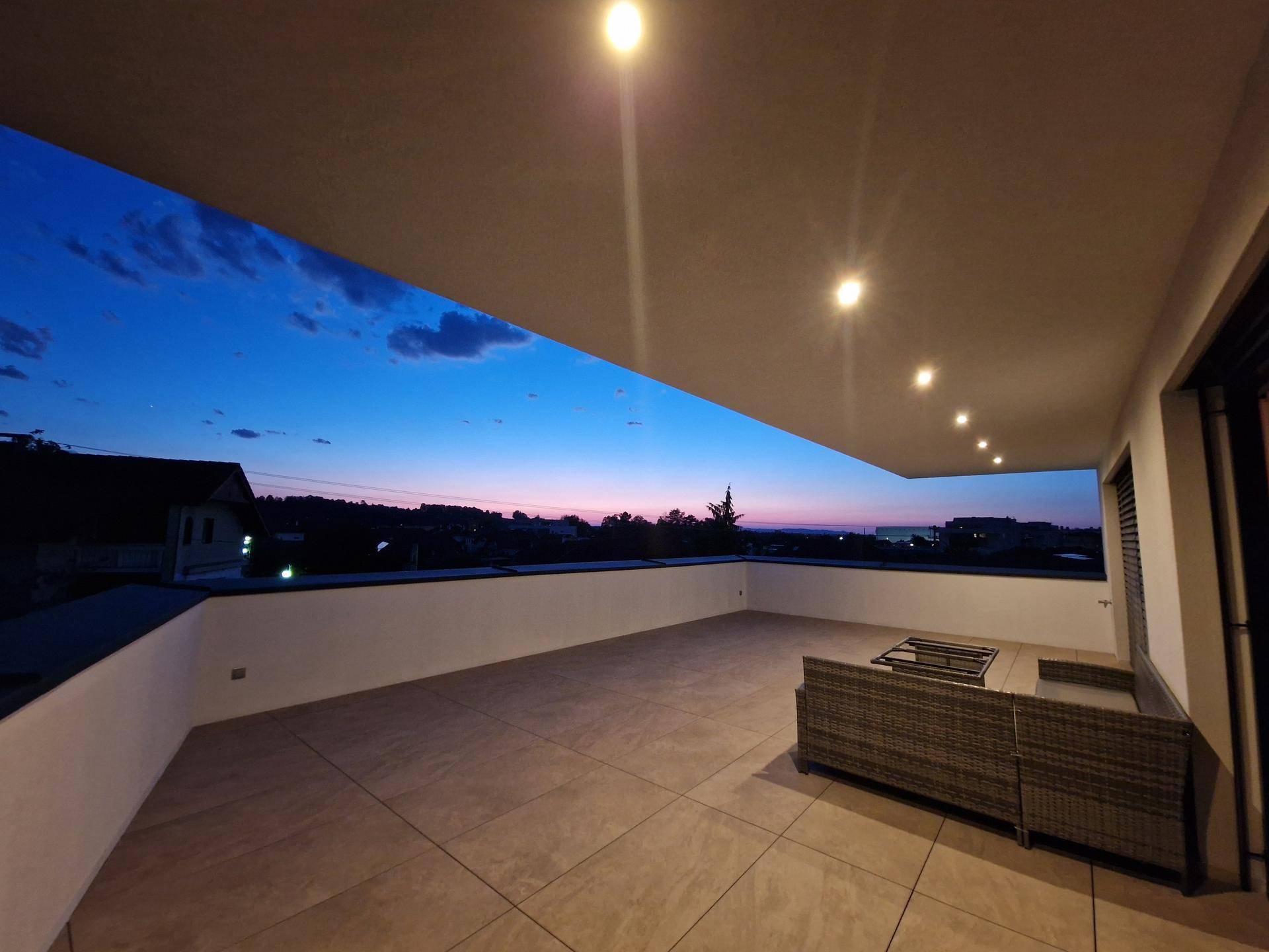 Abendliche Terrasse mit integrierter Beleuchtung und Loungemöbeln unter einem dämmernden Himmel.