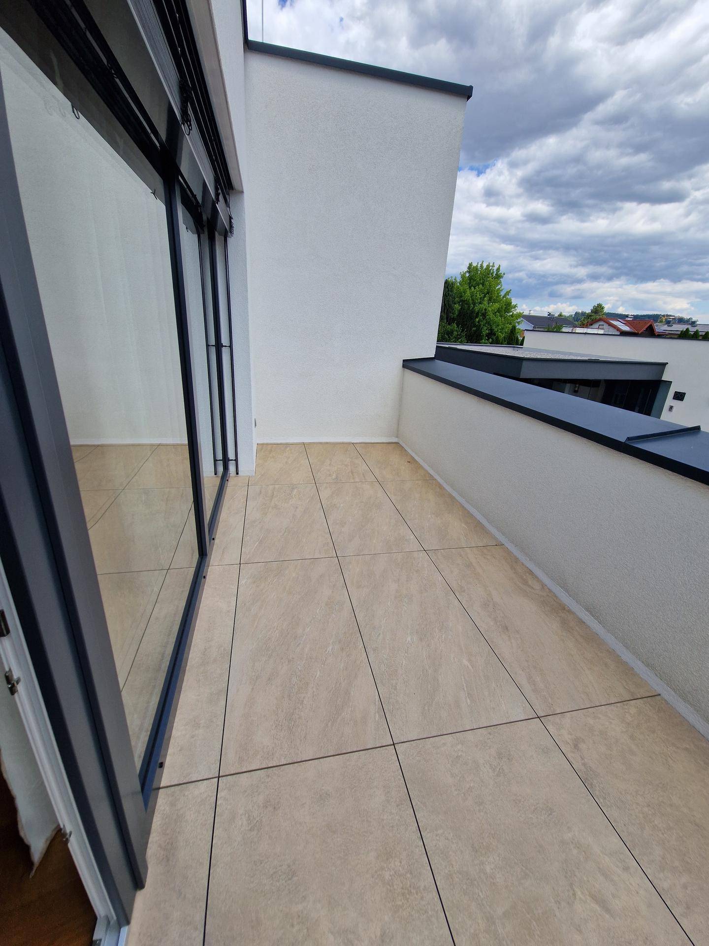 Geräumige Terrasse mit hellen Fliesen und weißer Brüstung unter bewölktem Himmel.