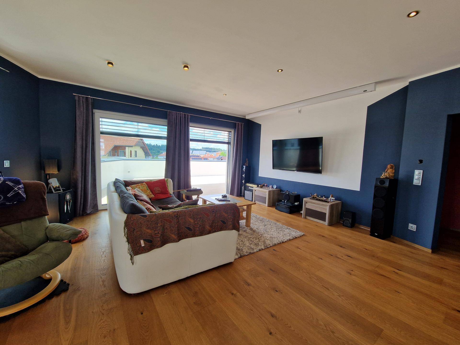 Helles Wohnzimmer mit Holzboden, blauen Wänden und Zugang zu einer großen Terrasse.