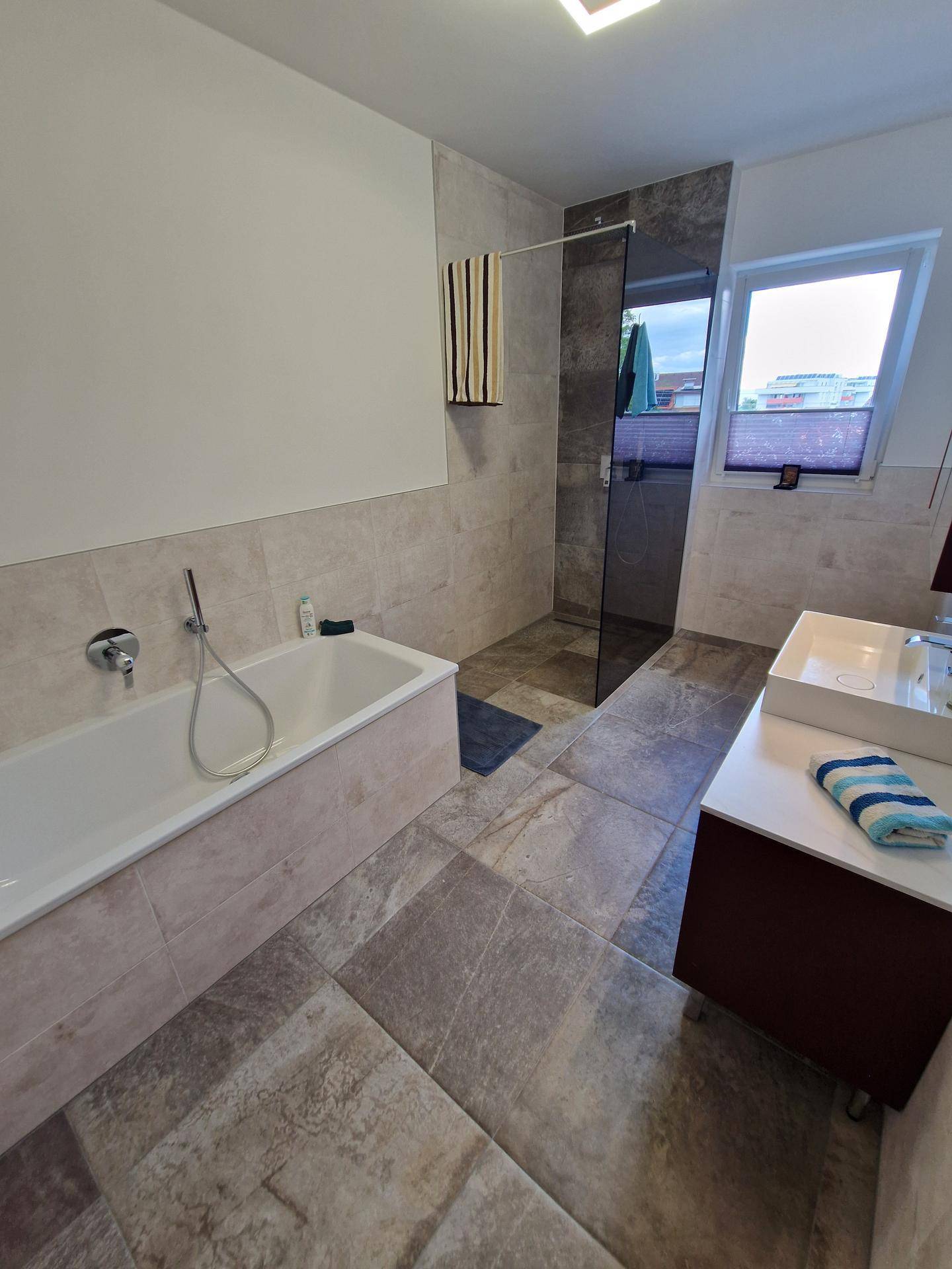 Detailansicht des Badezimmers mit moderner Badewanne und großer begehbarer Dusche.