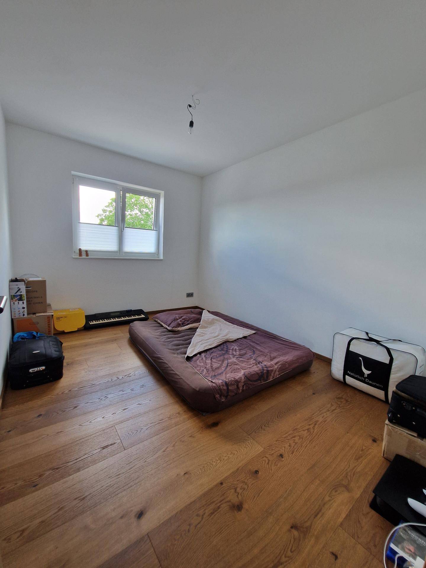 Helles Schlafzimmer mit Holzboden und einem Fenster, das viel Tageslicht hereinlässt.