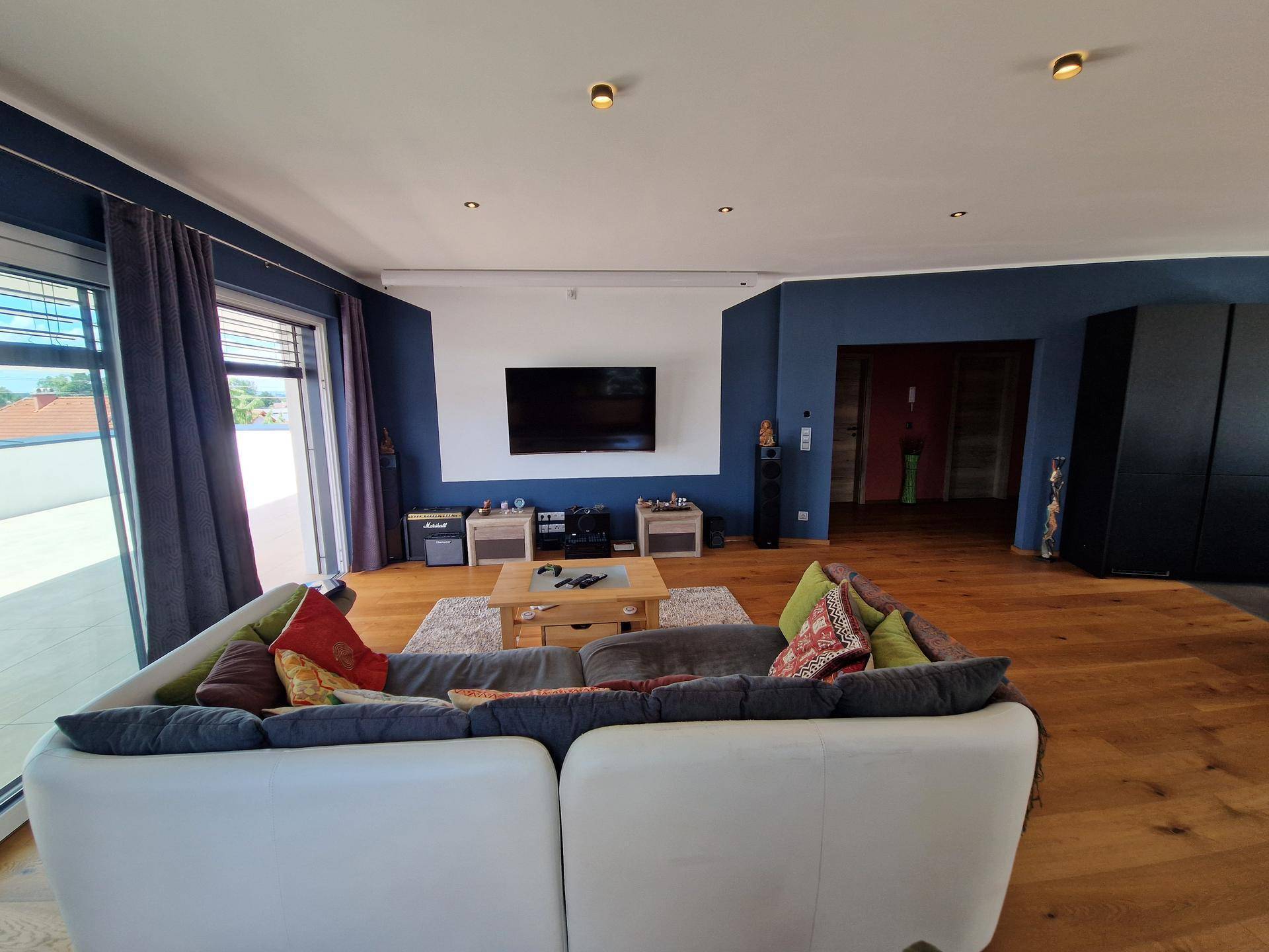Gemütliches Wohnzimmer mit großem Sofa, Wandfernseher und Holzboden.