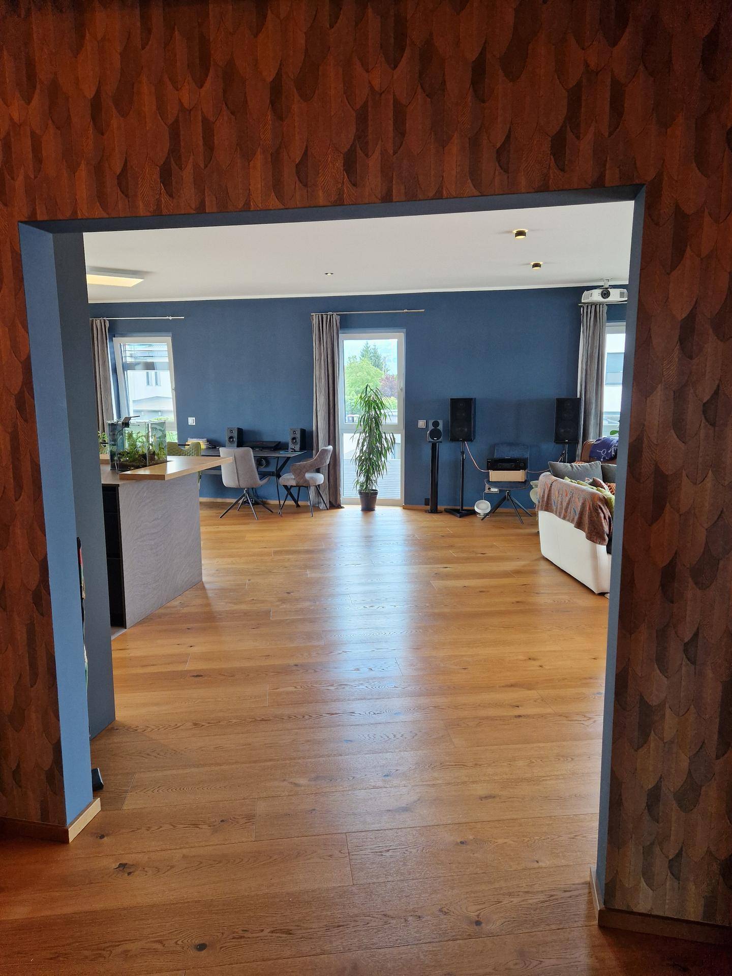 Offener Übergang vom Flur in den Wohnbereich mit Holzboden und blauen Wänden.