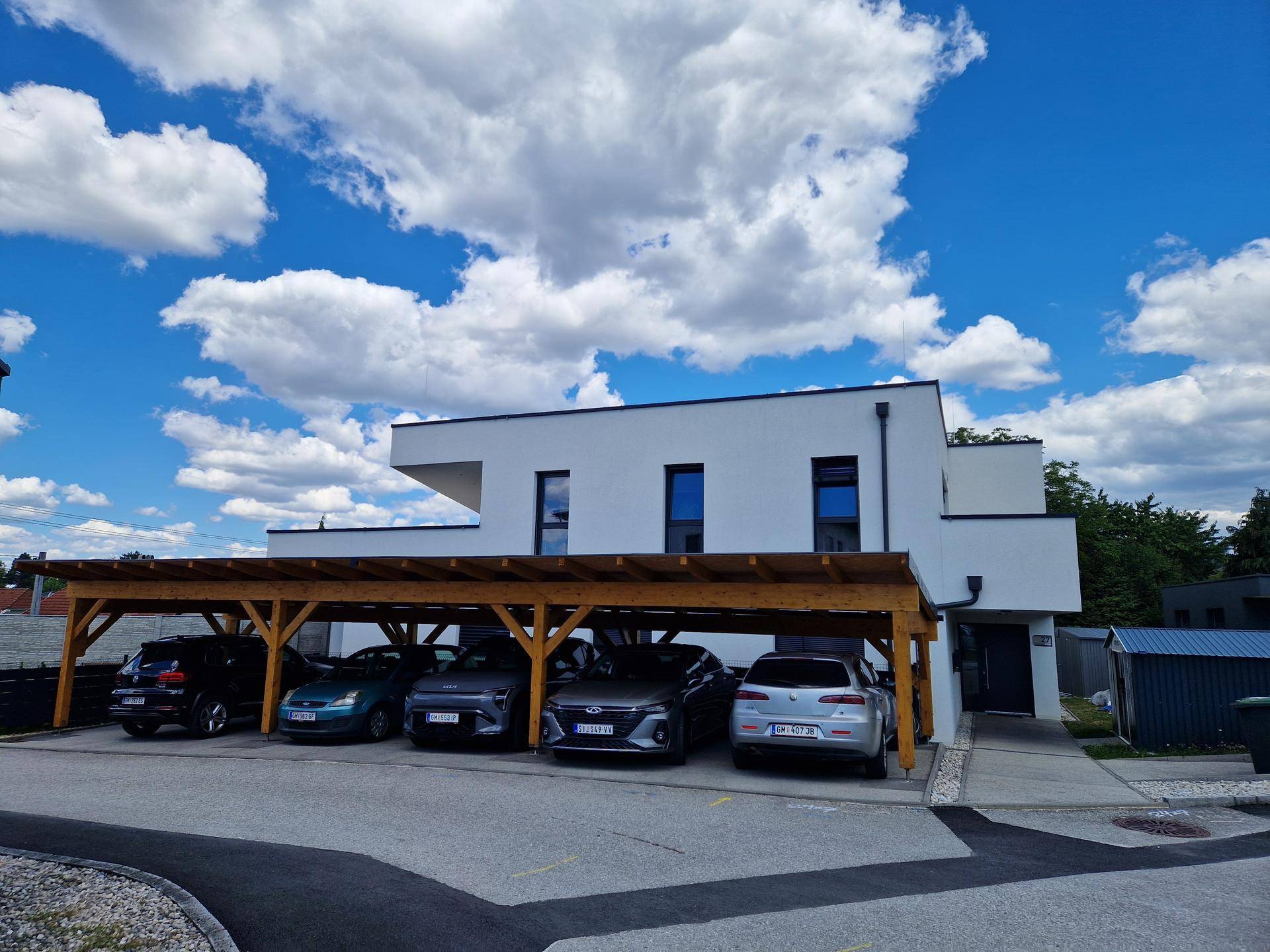 Moderne weiße Gebäudefassade mit einem Holzcarport und mehreren geparkten Autos.