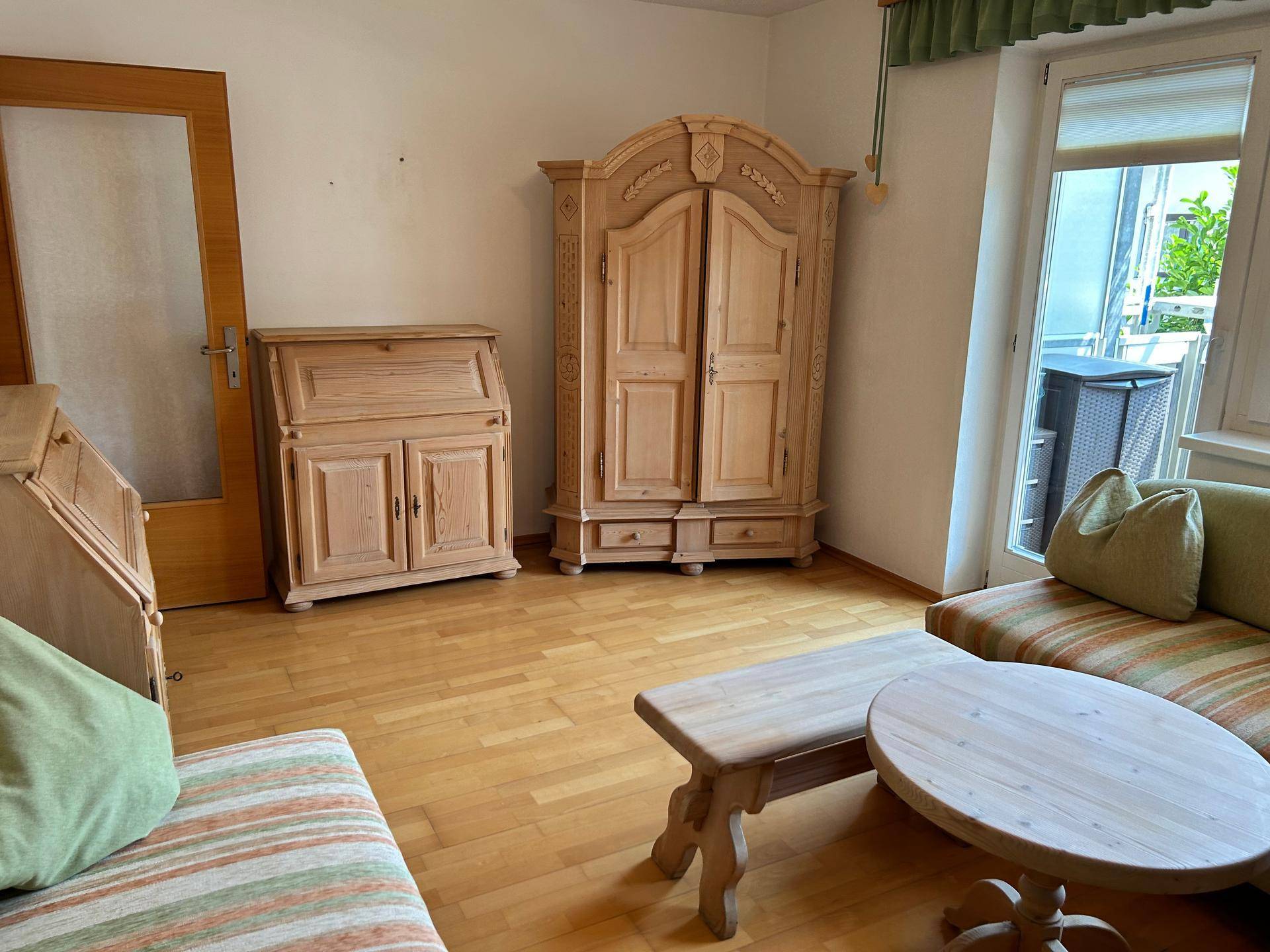 Heller Wohnraum mit großem Holzschrank, Schreibtisch und Zugang zum Außenbereich.