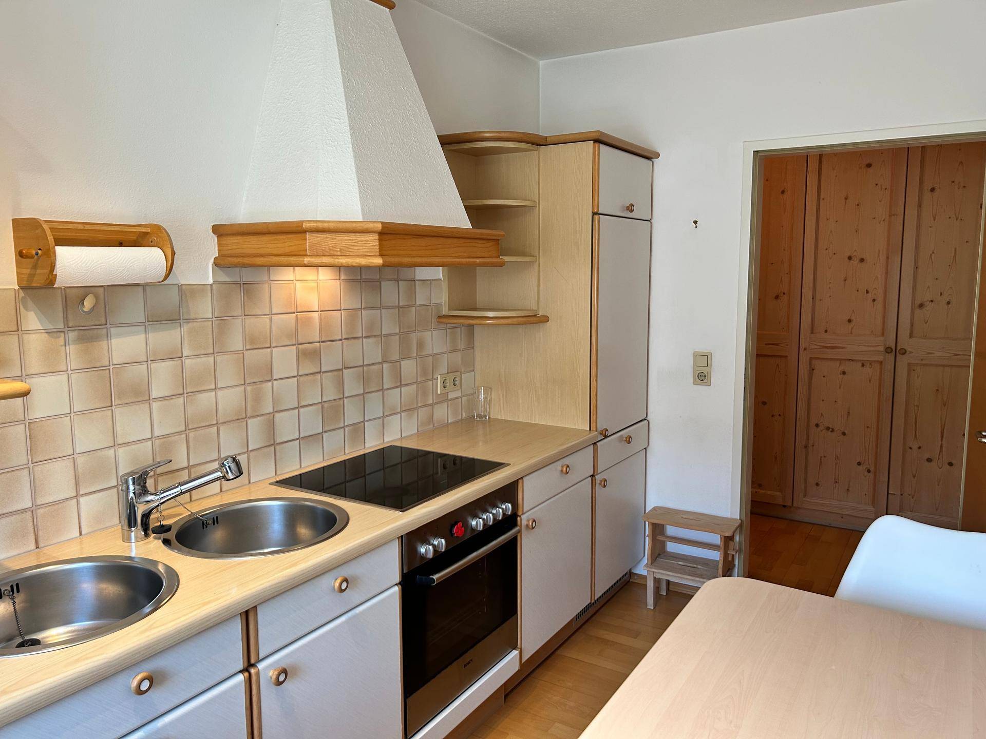 Funktionale Küche mit hellen Einbauschränken, Kochfeld und Backofen, sowie gefliestem Spritzschutz.