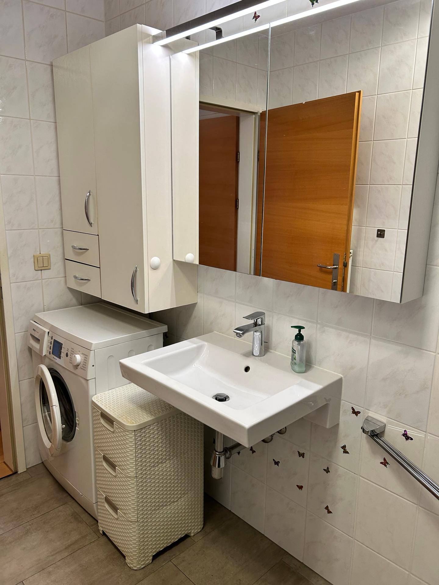 Badezimmer mit Waschmaschine, Waschbecken und Spiegelschrank, praktisch eingerichtet.