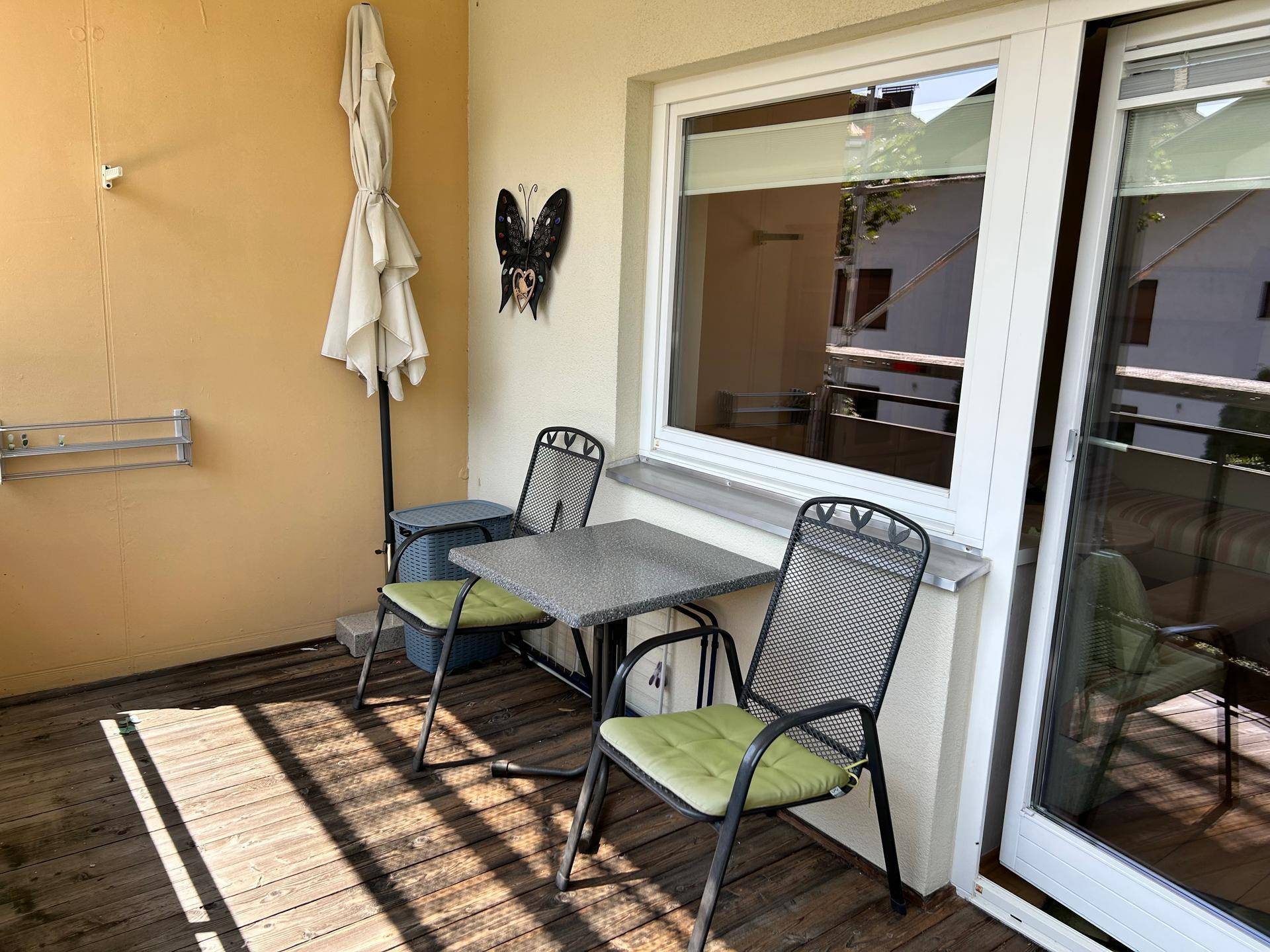 Gemütlicher Balkon mit Holzboden, Sitzgelegenheiten und Sonnenschirm für entspannte Stunden.