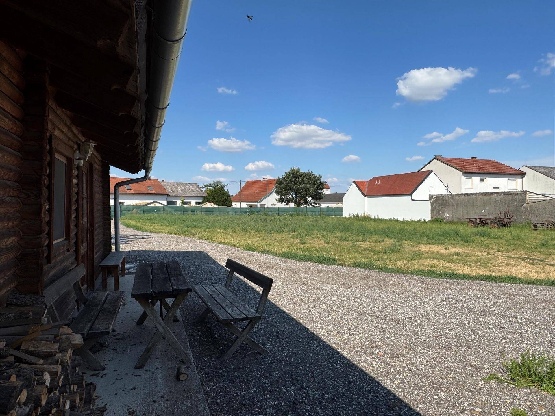 Rustikale Holzhütte mit einem einfachen Picknicktisch auf einem Kiesweg, umgeben von Natur.