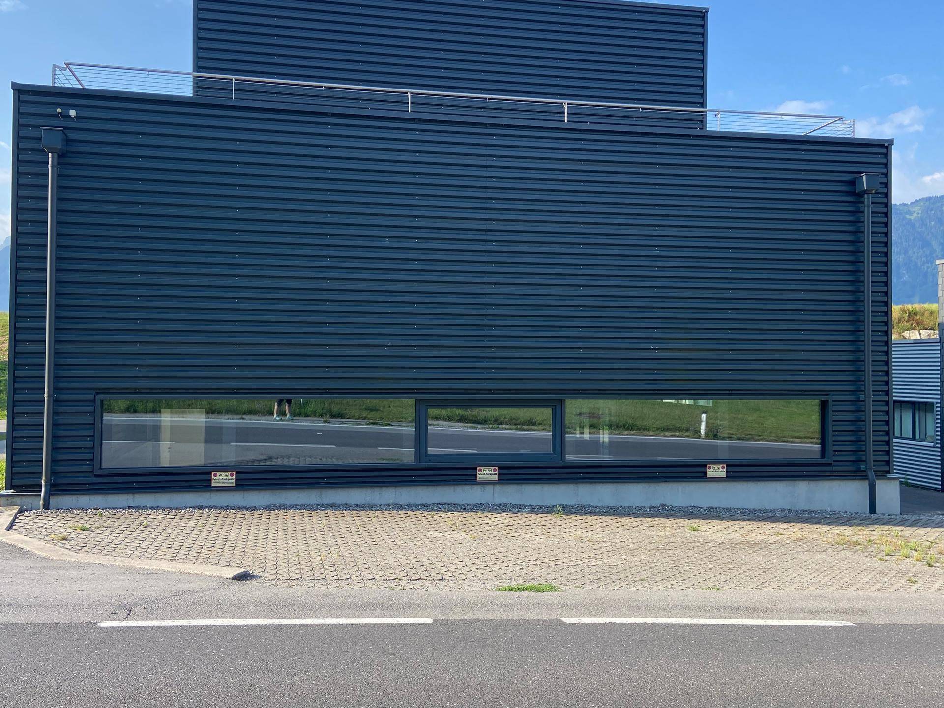 Vorderansicht eines modernen Geschäftsgebäudes mit langen, schmalen Fenstern und dunkler geriffelter Fassade.
