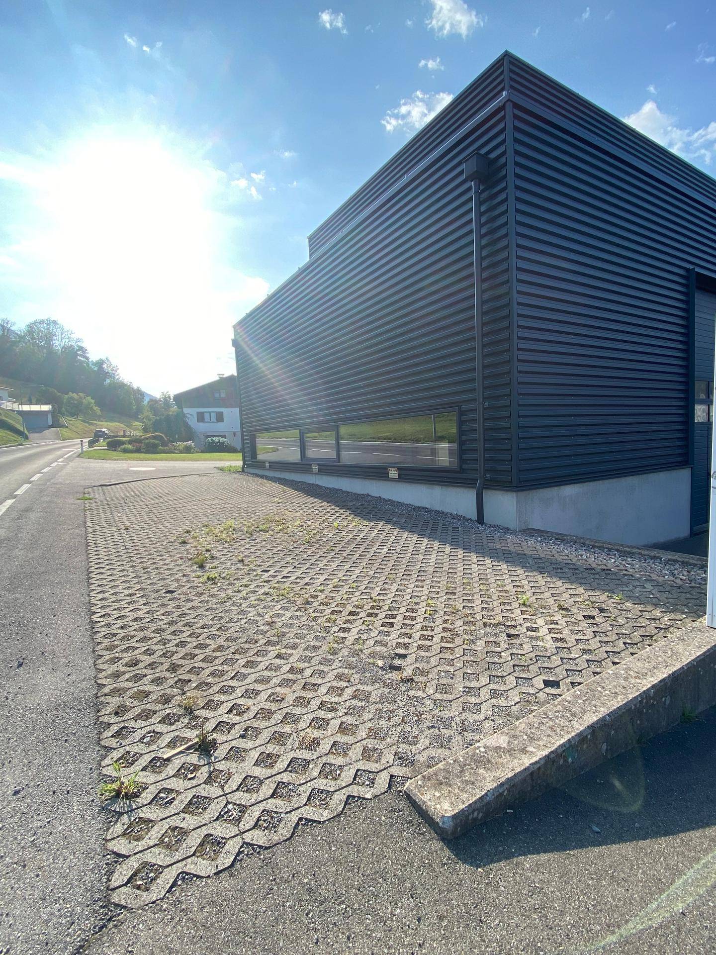 Außenansicht des Gebäudes mit einem großen Parkplatz aus Rasengittersteinen unter strahlendem Himmel.
