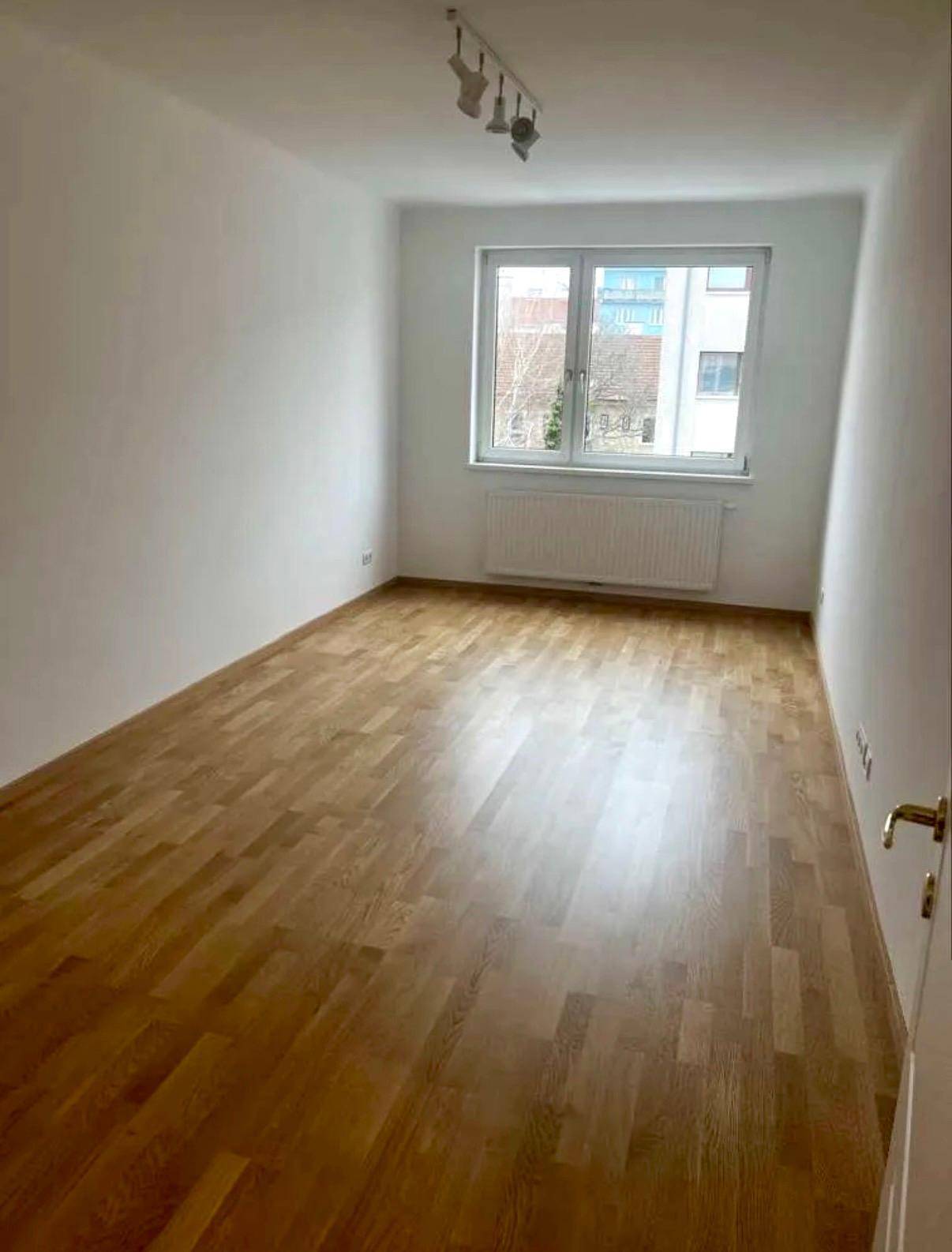 Helles Schlafzimmer mit Parkettboden, großem Fenster und Heizkörper, bereit zur individuellen Gestaltung.