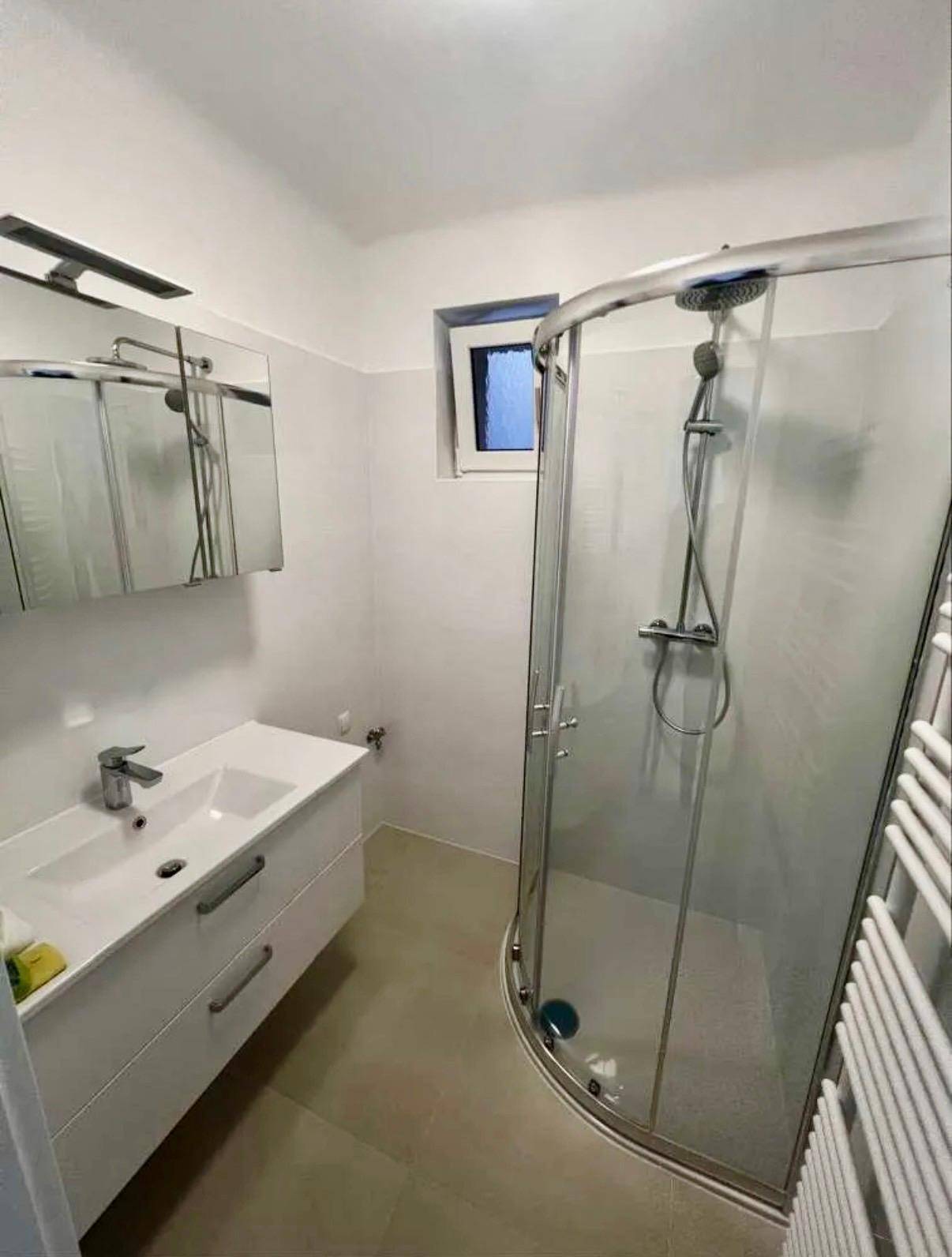 Modernes Badezimmer mit Duschkabine, Waschtisch, Spiegelschrank und beheiztem Handtuchhalter.
