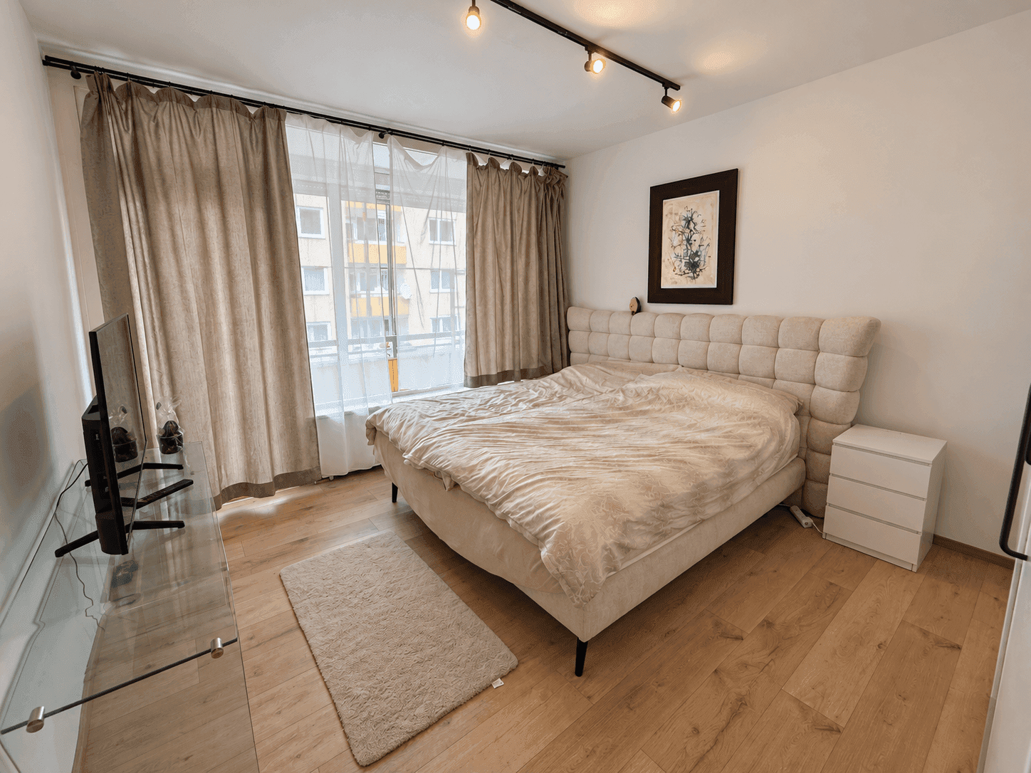 Helles Schlafzimmer mit großem Doppelbett, Parkettboden und Vorhängen für Privatsphäre.