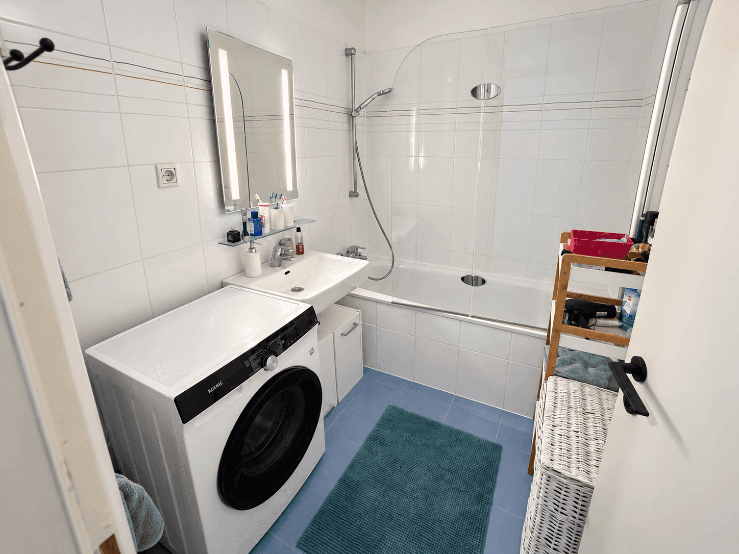 Modernes Badezimmer mit Badewanne, Waschmaschine und beleuchtetem Spiegelschrank.