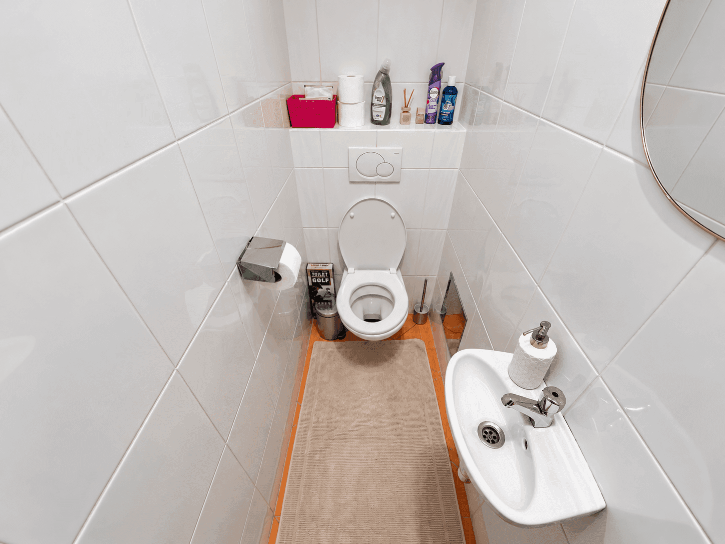 Kleines Gäste-WC mit weißen Fliesen, wandhängender Toilette und kompaktem Waschbecken.