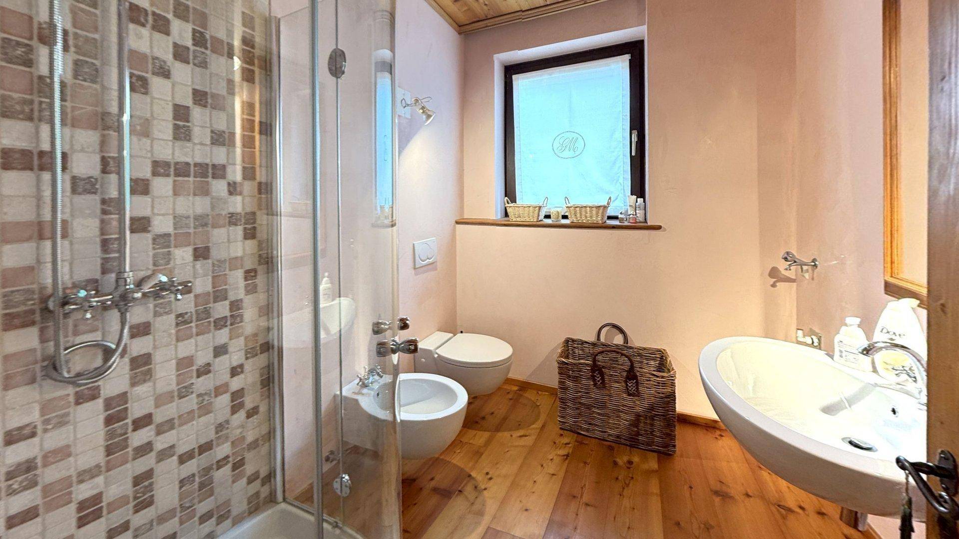 Badezimmer mit Dusche, WC, Bidet, Waschbecken und einem Fenster für Tageslicht.
