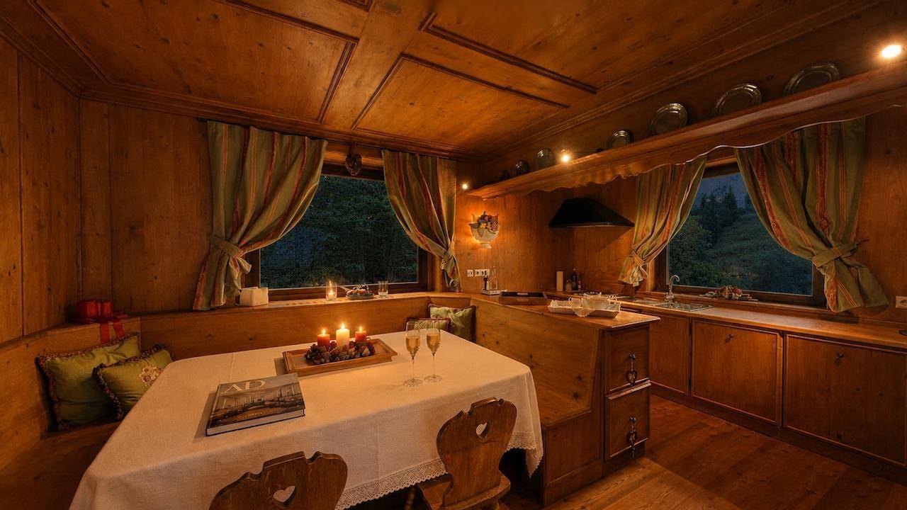 Gemütliche Holzküche mit Essbereich, abendlicher Beleuchtung und Blick in die dunkle Natur.