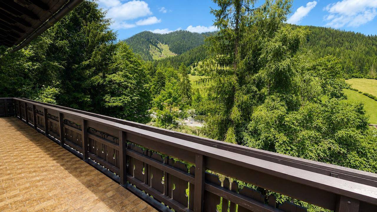 Weitläufiger Blick vom Balkon auf die grünen Wälder und Berge unter blauem Himmel.