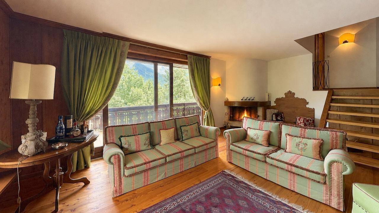 Gemütliches Wohnzimmer mit Kamin, bequemen Sofas und Zugang zum Balkon mit Bergblick.