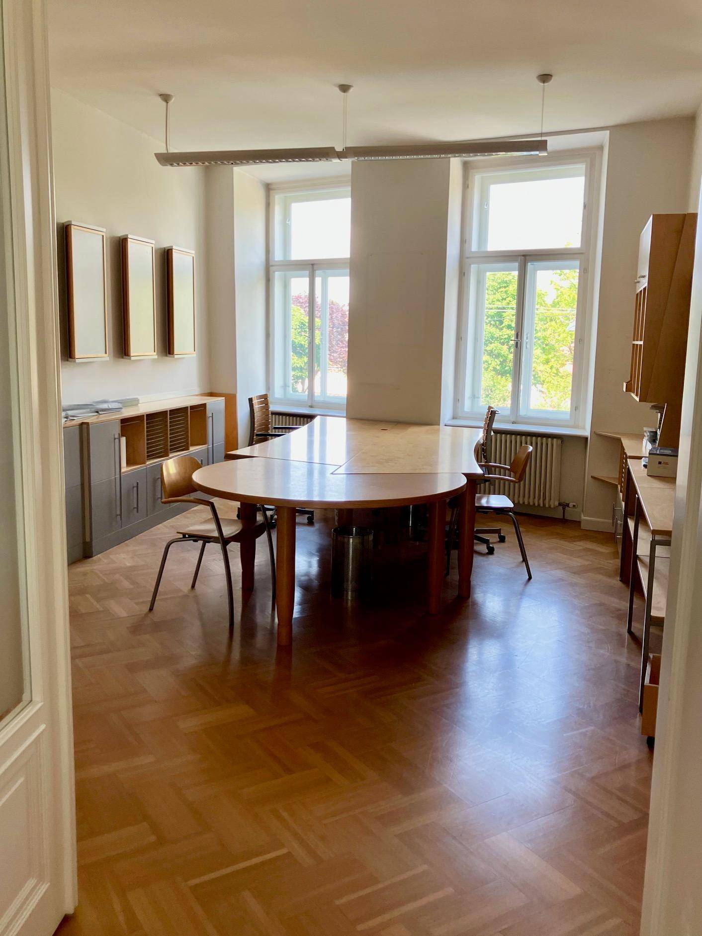 Heller Büroraum mit großem Holztisch, Stühlen und Blick auf die Umgebung durch die Fenster.