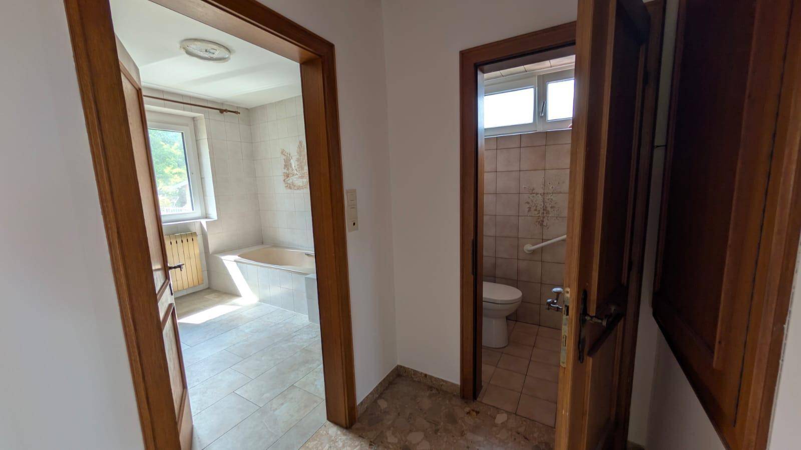 Flur mit Zugang zu Badezimmer und separater Toilette, mit Holztüren und Fliesenboden.