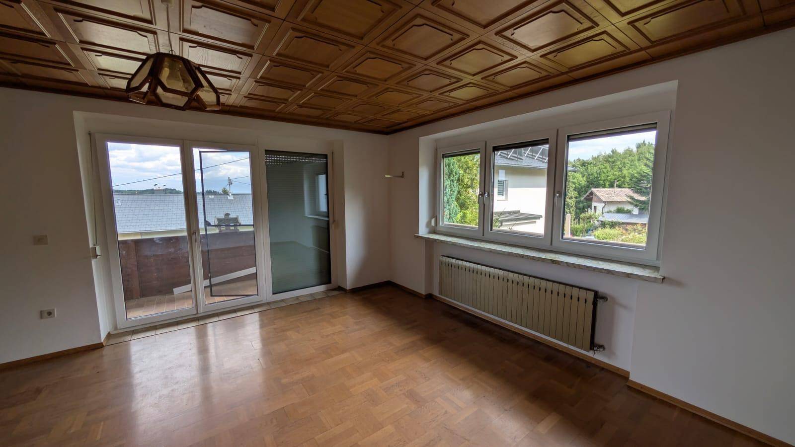 Geräumiges Wohnzimmer mit Parkettboden, Holzdecke und großen Fenstern mit Ausblick.