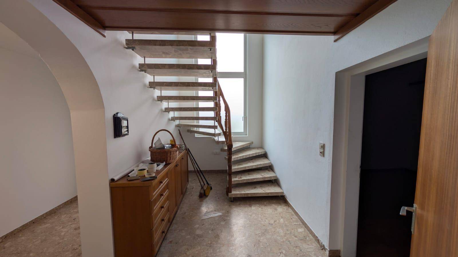 Heller Flur mit geschwungener Treppe, großem Fenster und Stauraum unter der Treppe.