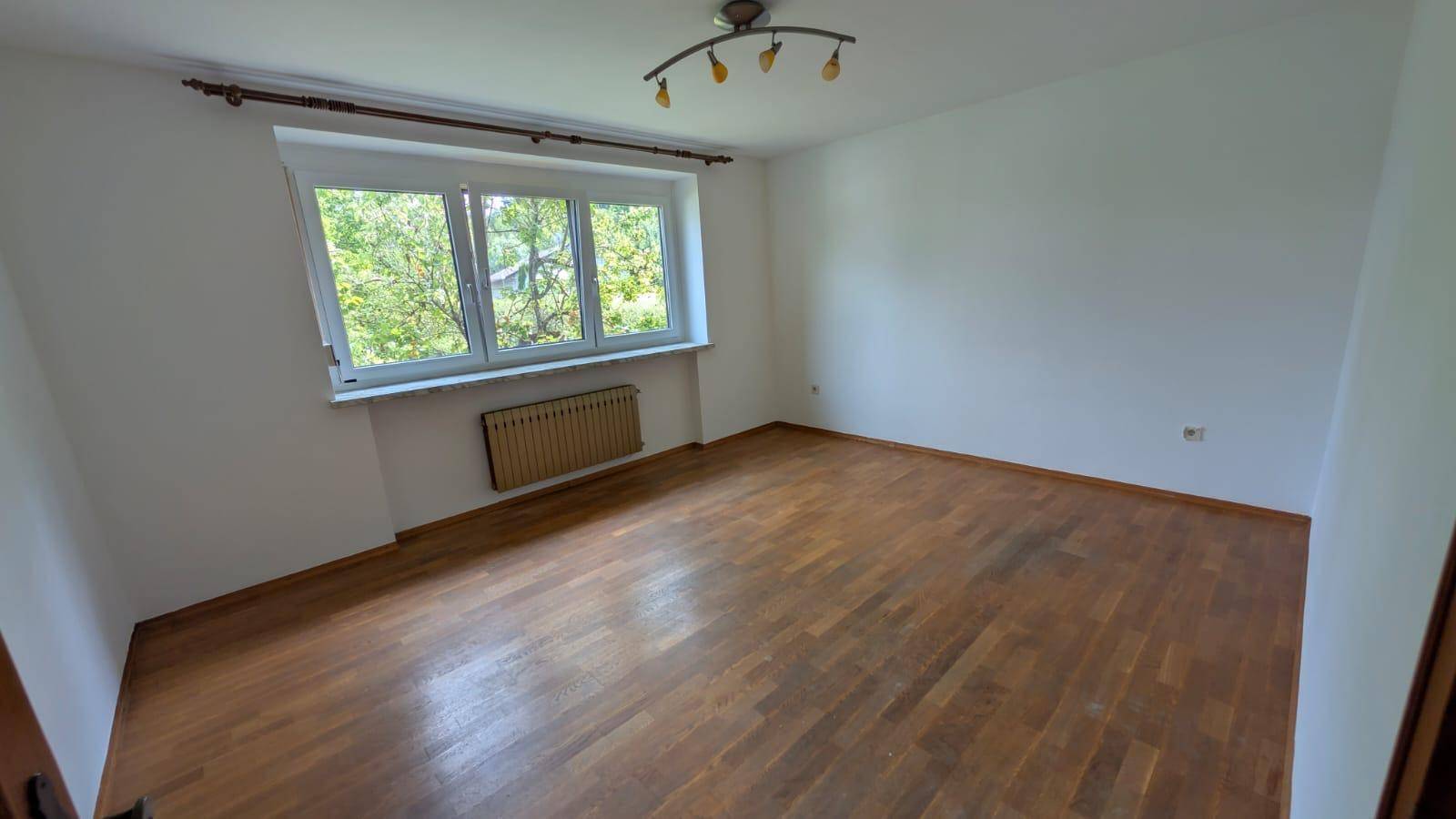 Geräumiges Schlafzimmer mit Parkettboden und großem Fenster, das viel Tageslicht hereinlässt.