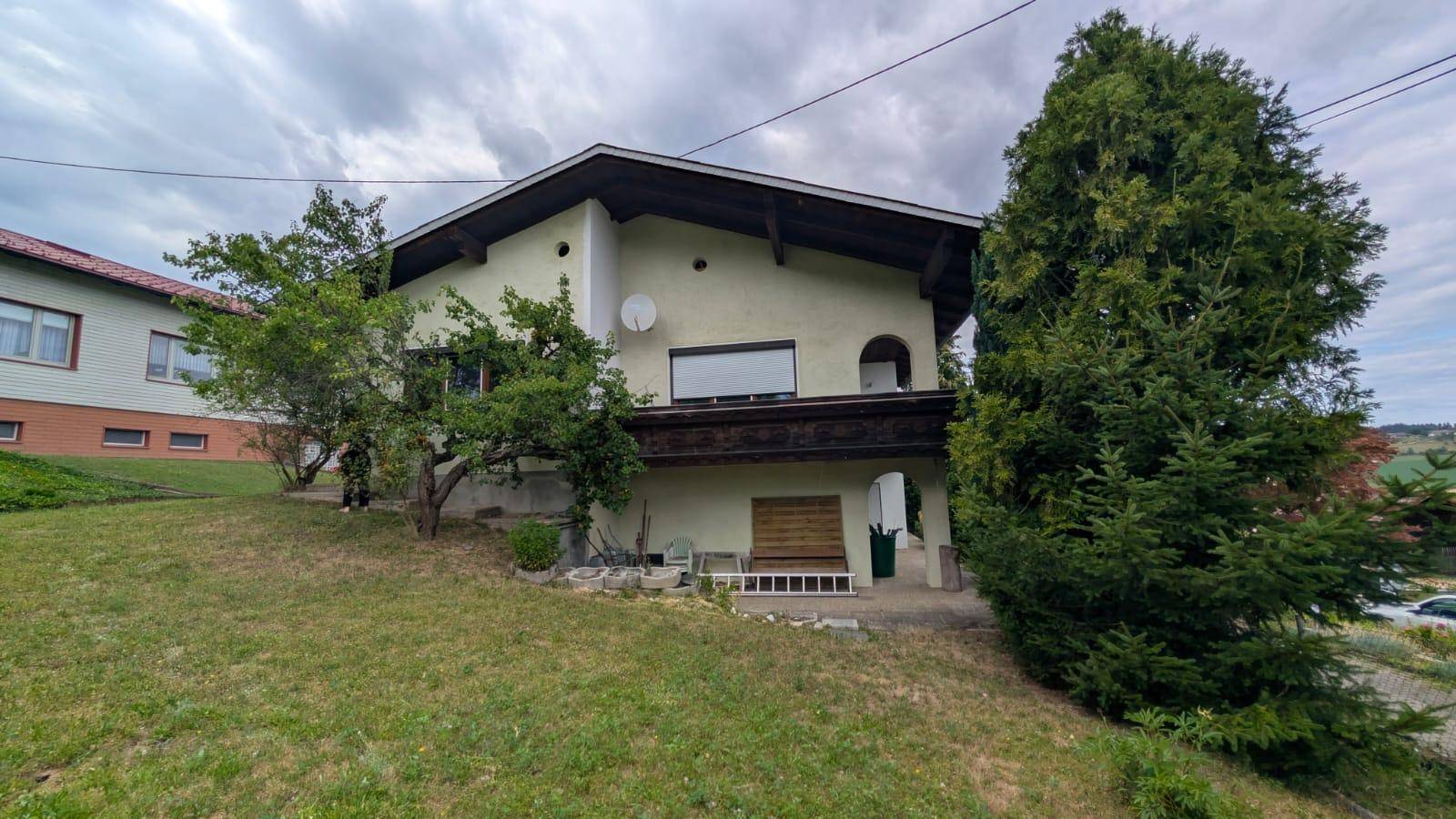 Seitenansicht des Hauses mit Balkon und Zugang zum Gartenbereich auf einem Hanggrundstück.