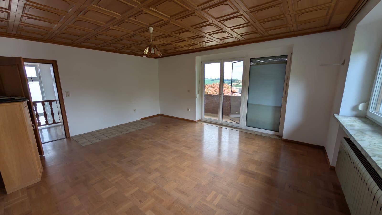 Helles Wohnzimmer mit Parkettboden, Holzdecke und Zugang zu einem Balkon.