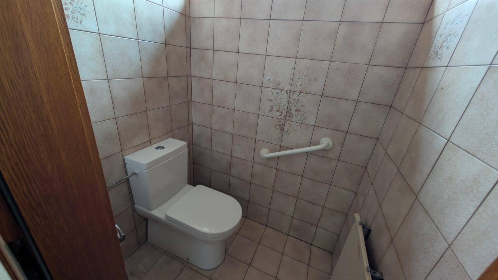 Separate Toilette mit Wandfliesen und Haltegriff für zusätzliche Sicherheit.