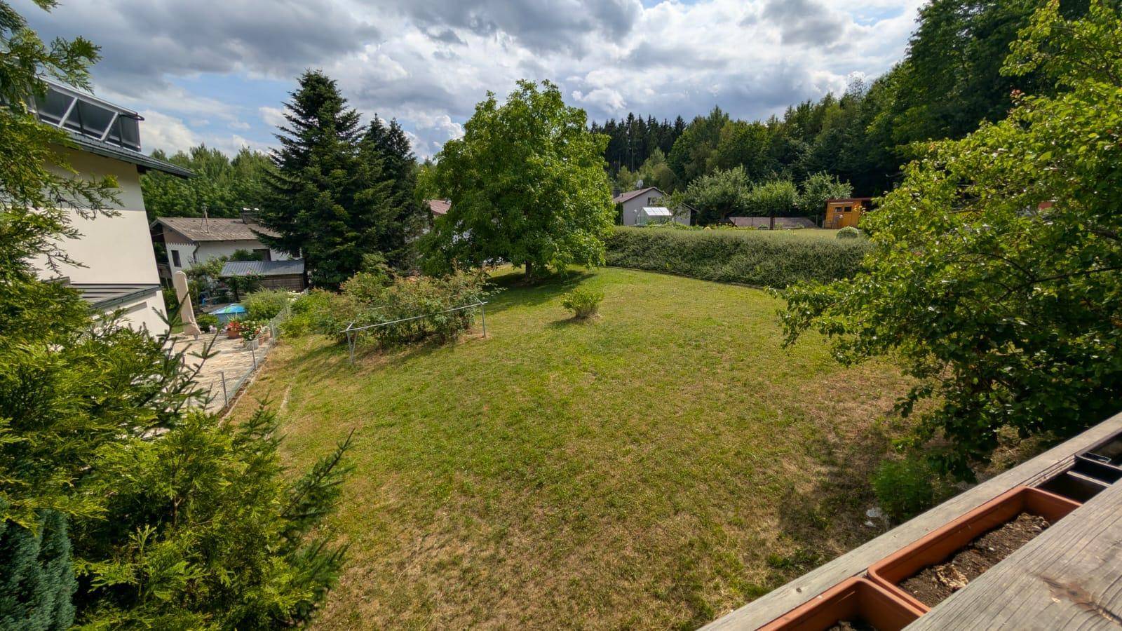 Panoramablick über den weitläufigen Garten mit Bäumen und umliegender Landschaft an einem sonnigen Tag.