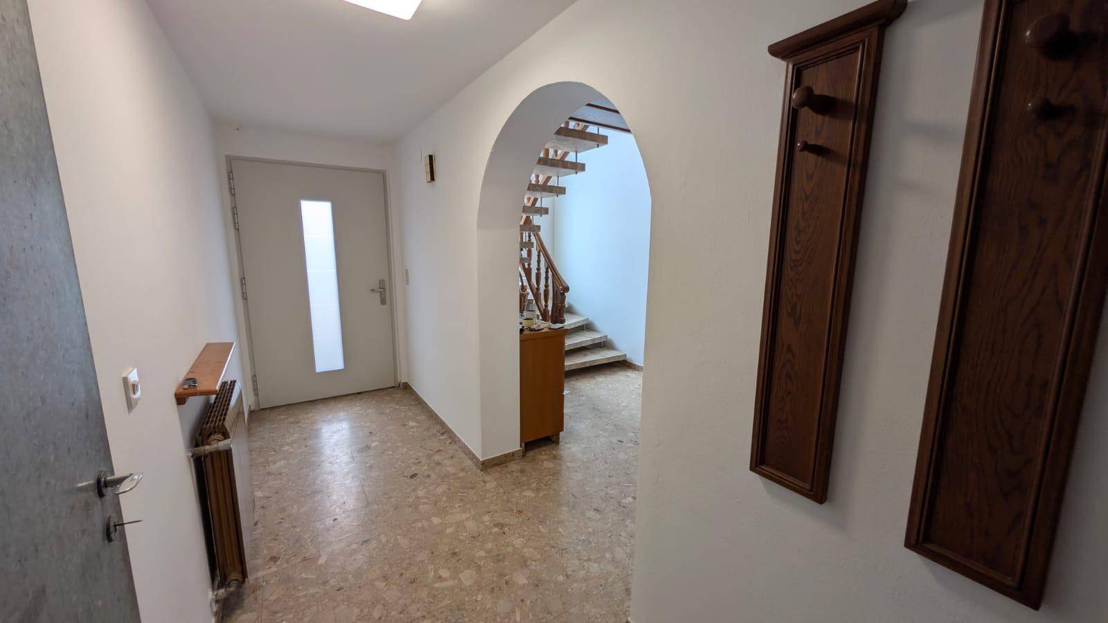 Eingangsbereich mit Fliesenboden, Garderobe und Blick auf die geschwungene Treppe.