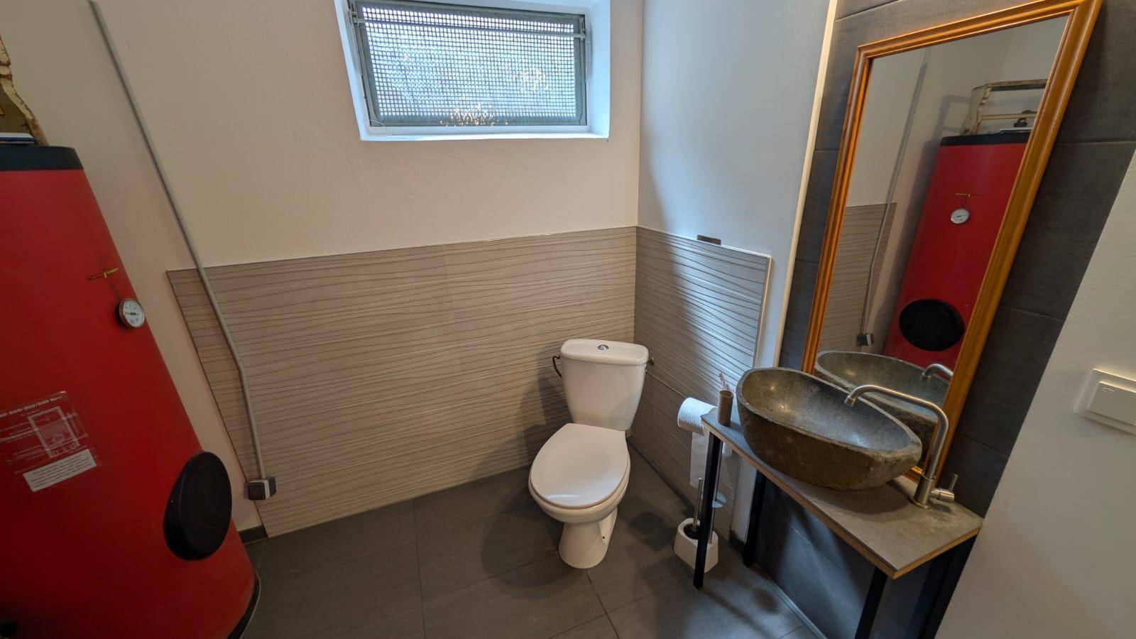 Einfache Toilette im Kellerbereich mit Waschbecken und Spiegel.