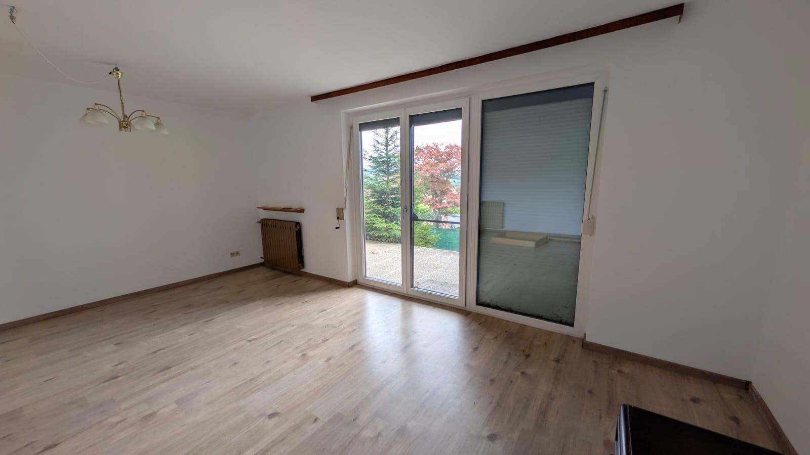 Helles Wohnzimmer mit Laminatboden und Zugang zu einem Balkon.