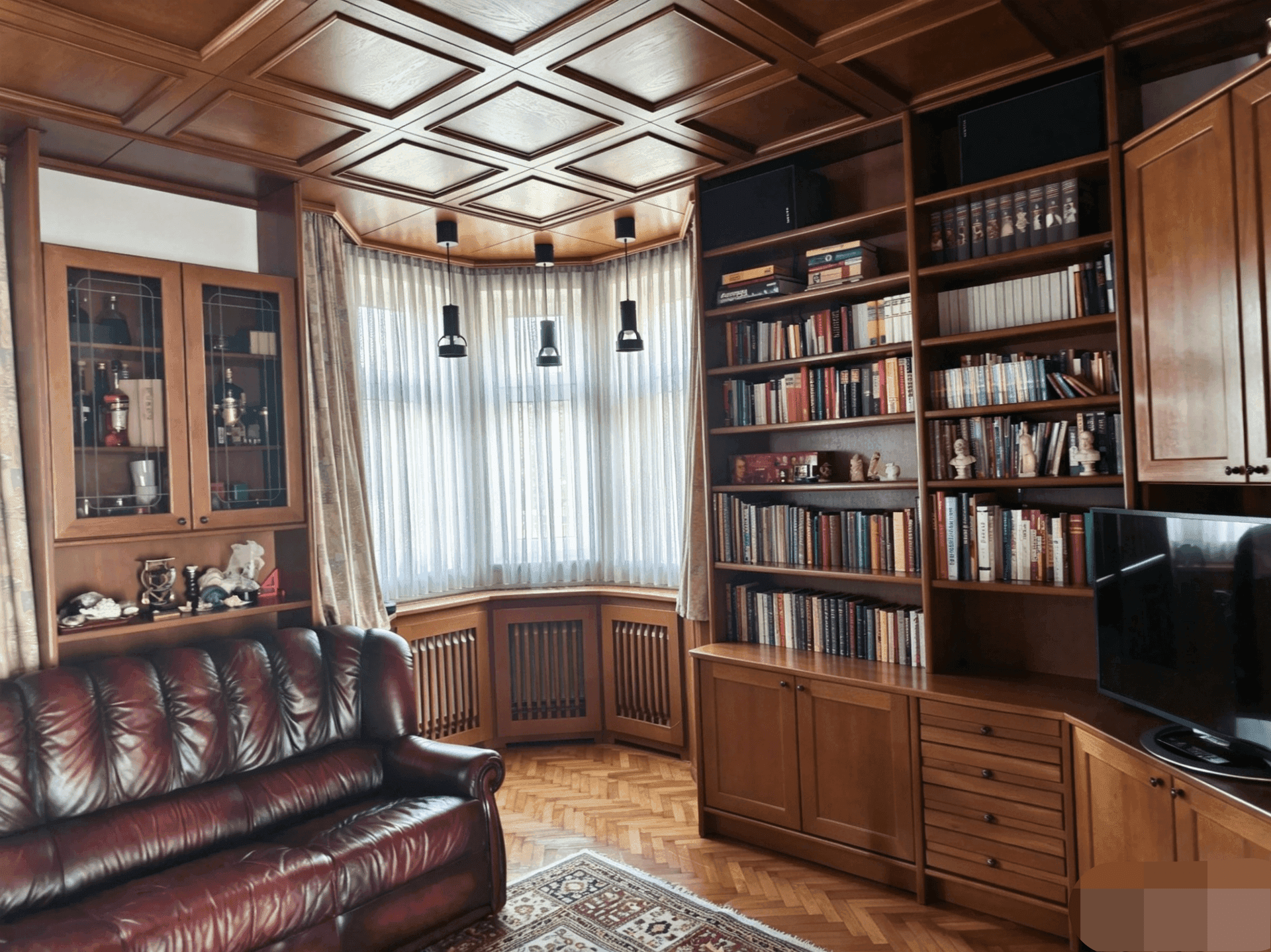 Gemütlicher Wohnbereich mit eingebauten Holzregalen, Ledersofa und Erkerfenster.
