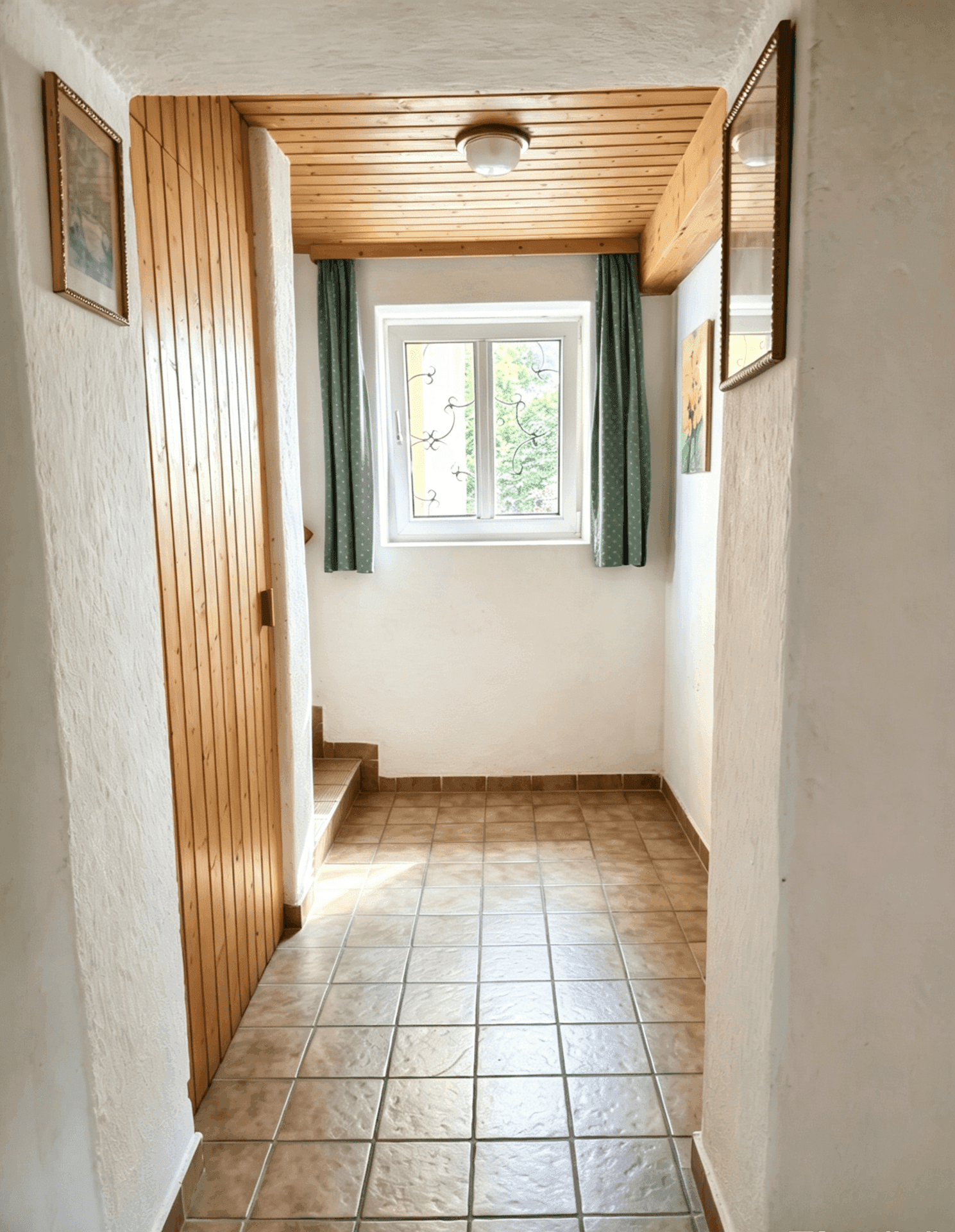 Heller Flur mit Fliesenboden, Holzdecke und einem Fenster mit grünen Vorhängen.