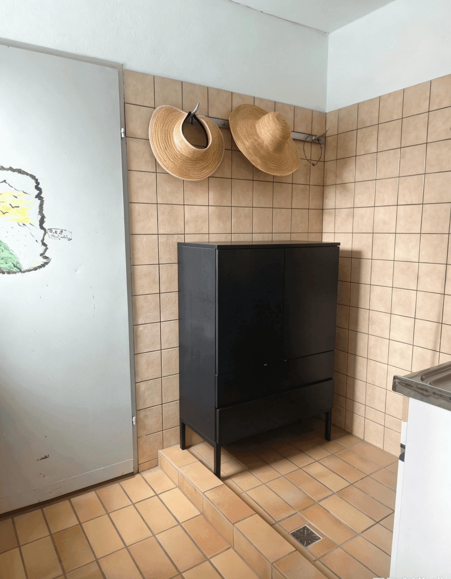 Umkleidebereich mit Fliesenwänden, Fliesenboden und einem schwarzen Schrank.