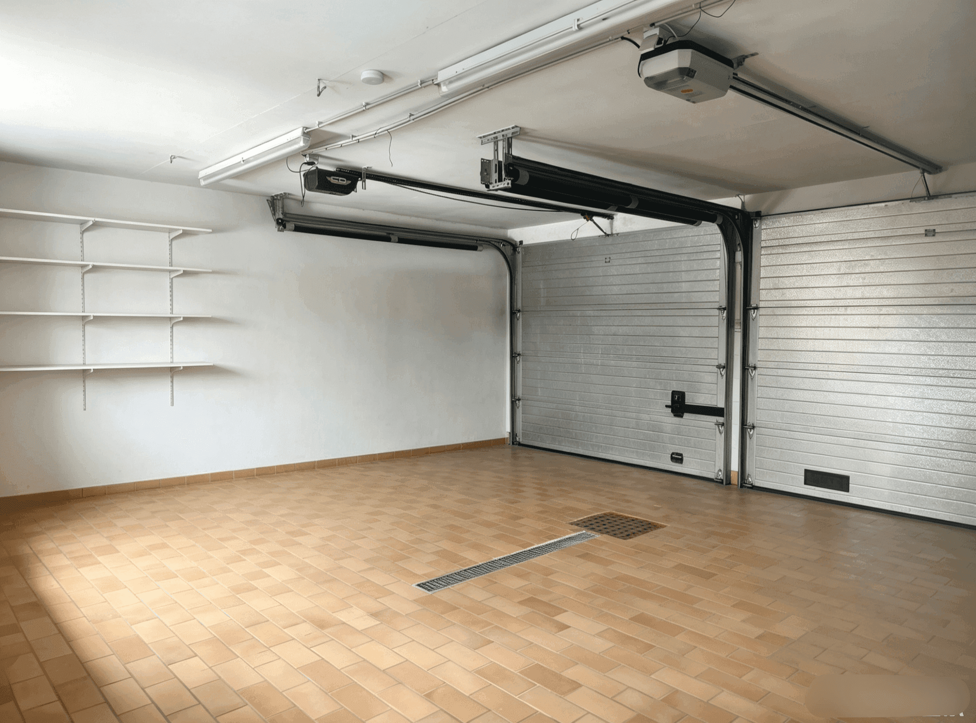 Geräumige Garage mit zwei Rolltoren, Fliesenboden und Wandregalen.