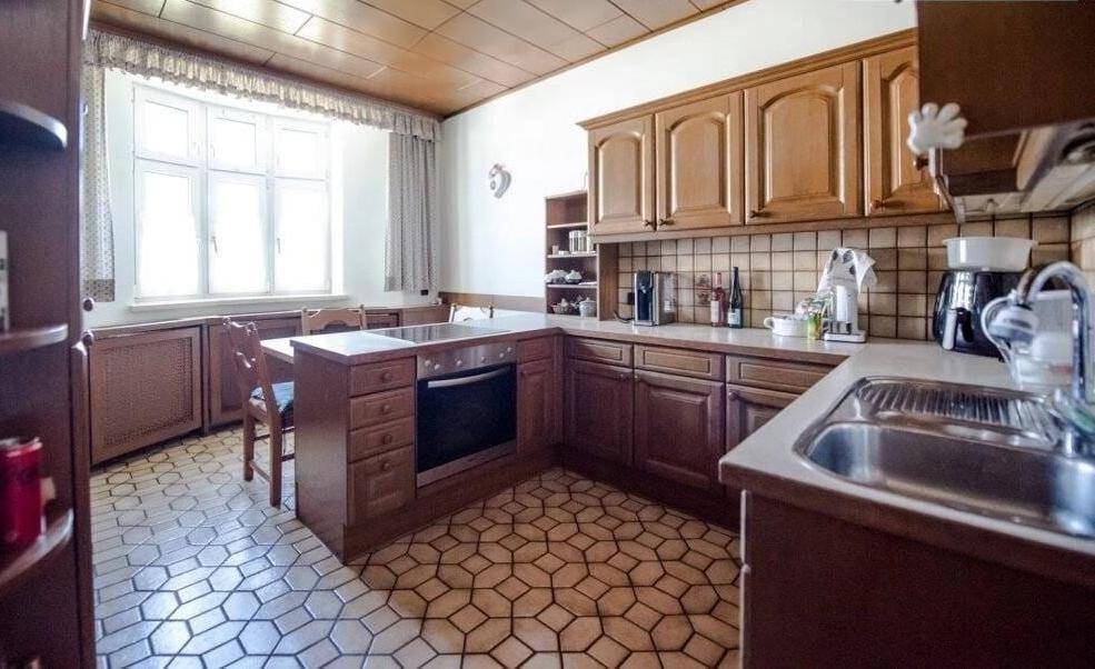 Klassische Küche mit Holzschränken, Backofen, Spüle und gemustertem Fliesenboden.